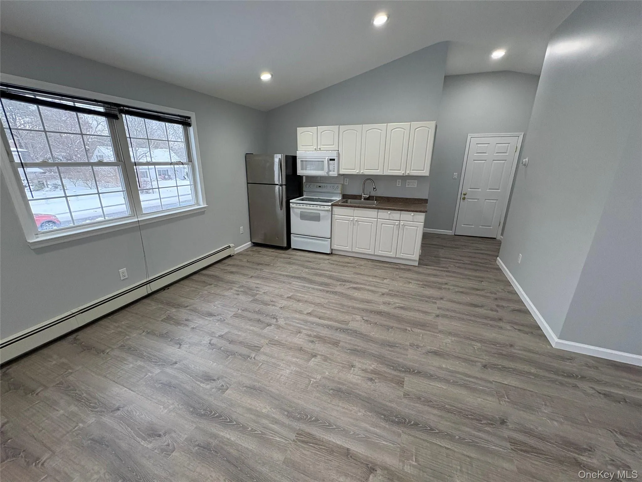 Kitchen with white cabinetry, a baseboard radiator, white appliances, light wood-style floors, and dark countertops Kitchen with white cabinetry, a baseboard radiator, white appliances, light wood-style floors, and dark countertops