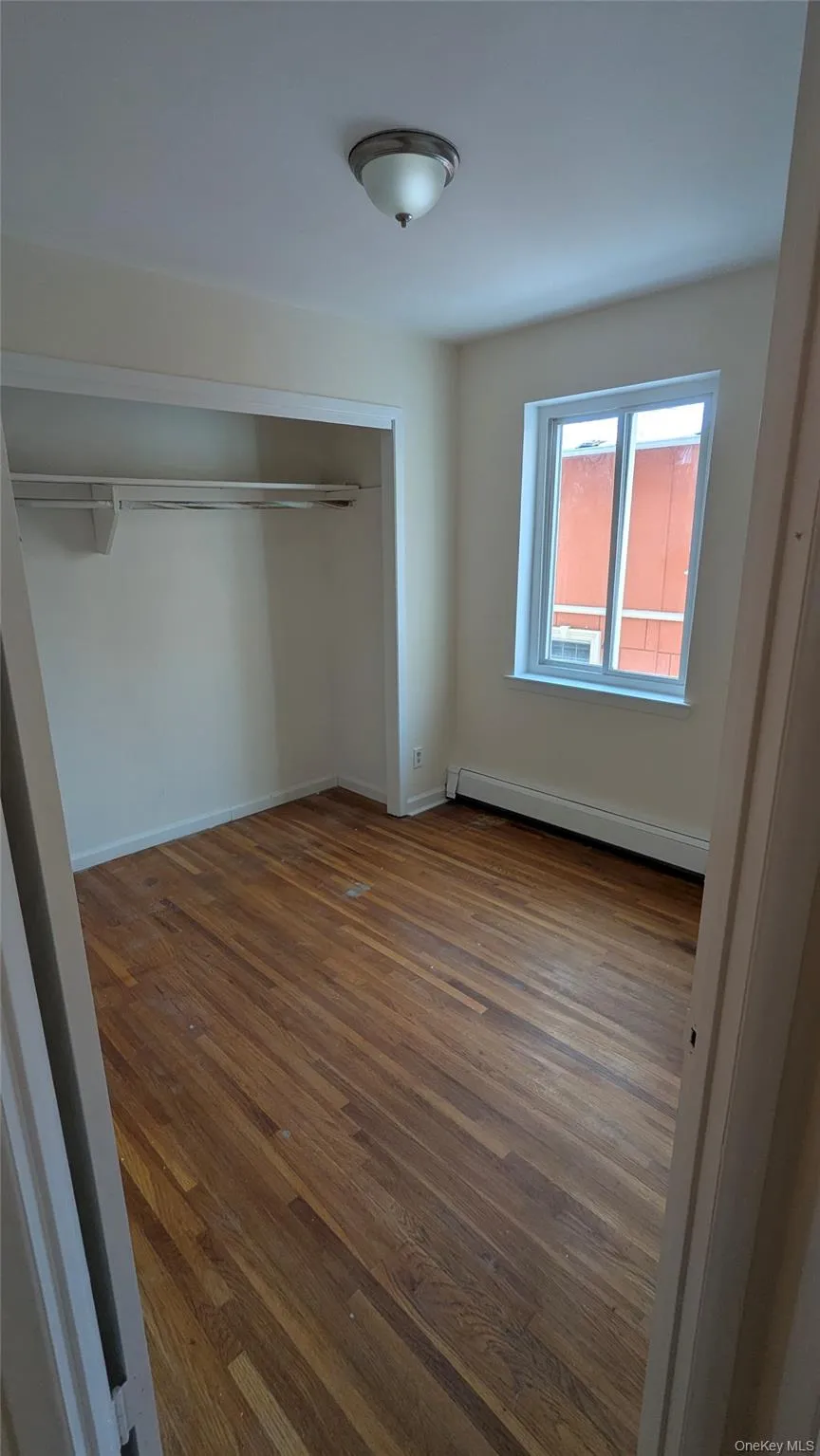 Unfurnished bedroom with dark wood-type flooring, a closet, and baseboard heating Unfurnished bedroom with dark wood-type flooring, a closet, and baseboard heating