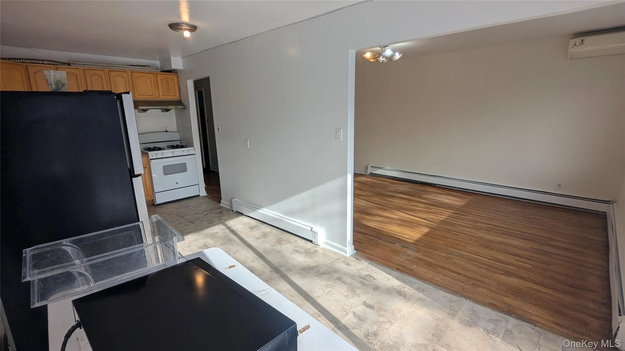 Kitchen featuring baseboard heating, white gas range oven, a wall unit AC, and light wood-type flooring Kitchen featuring baseboard heating, white gas range oven, a wall unit AC, and light wood-type flooring