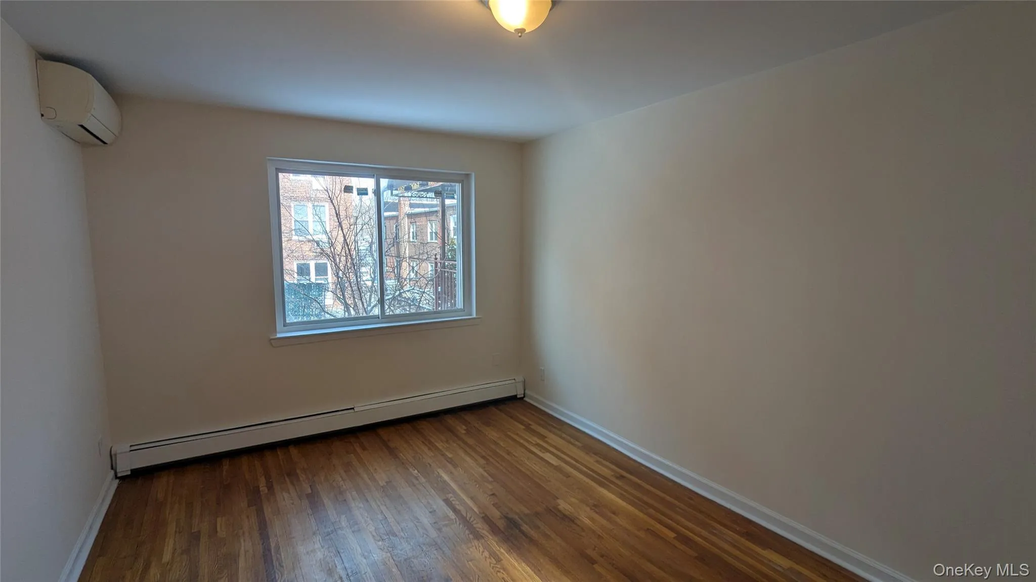 Empty room with a baseboard radiator, dark wood-style flooring, and an AC wall unit Empty room with a baseboard radiator, dark wood-style flooring, and an AC wall unit