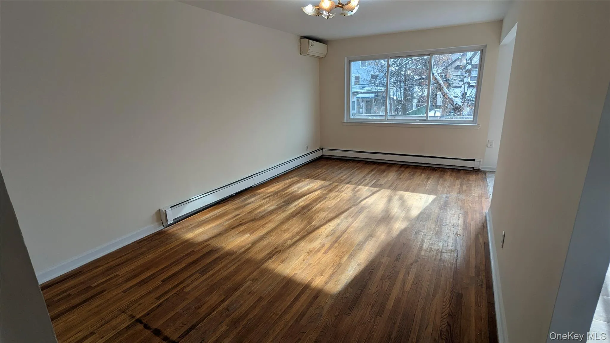 Empty room with baseboard heating, light wood finished floors, and a wall unit AC Empty room with baseboard heating, light wood finished floors, and a wall unit AC