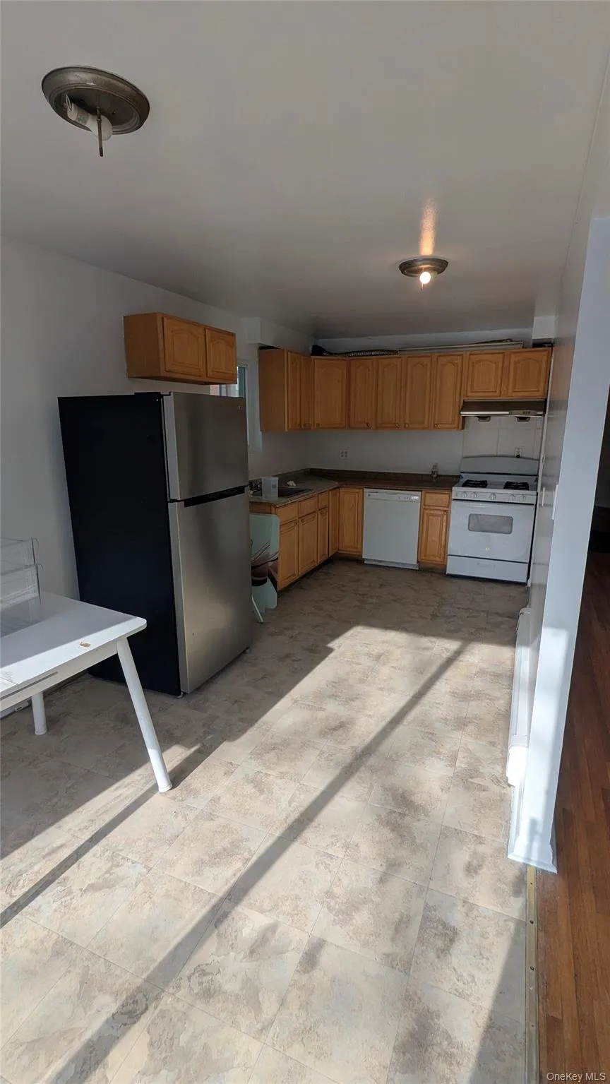 Kitchen featuring white appliances, under cabinet range hood, brown cabinetry, dark countertops, and light floors Kitchen featuring white appliances, under cabinet range hood, brown cabinetry, dark countertops, and light floors