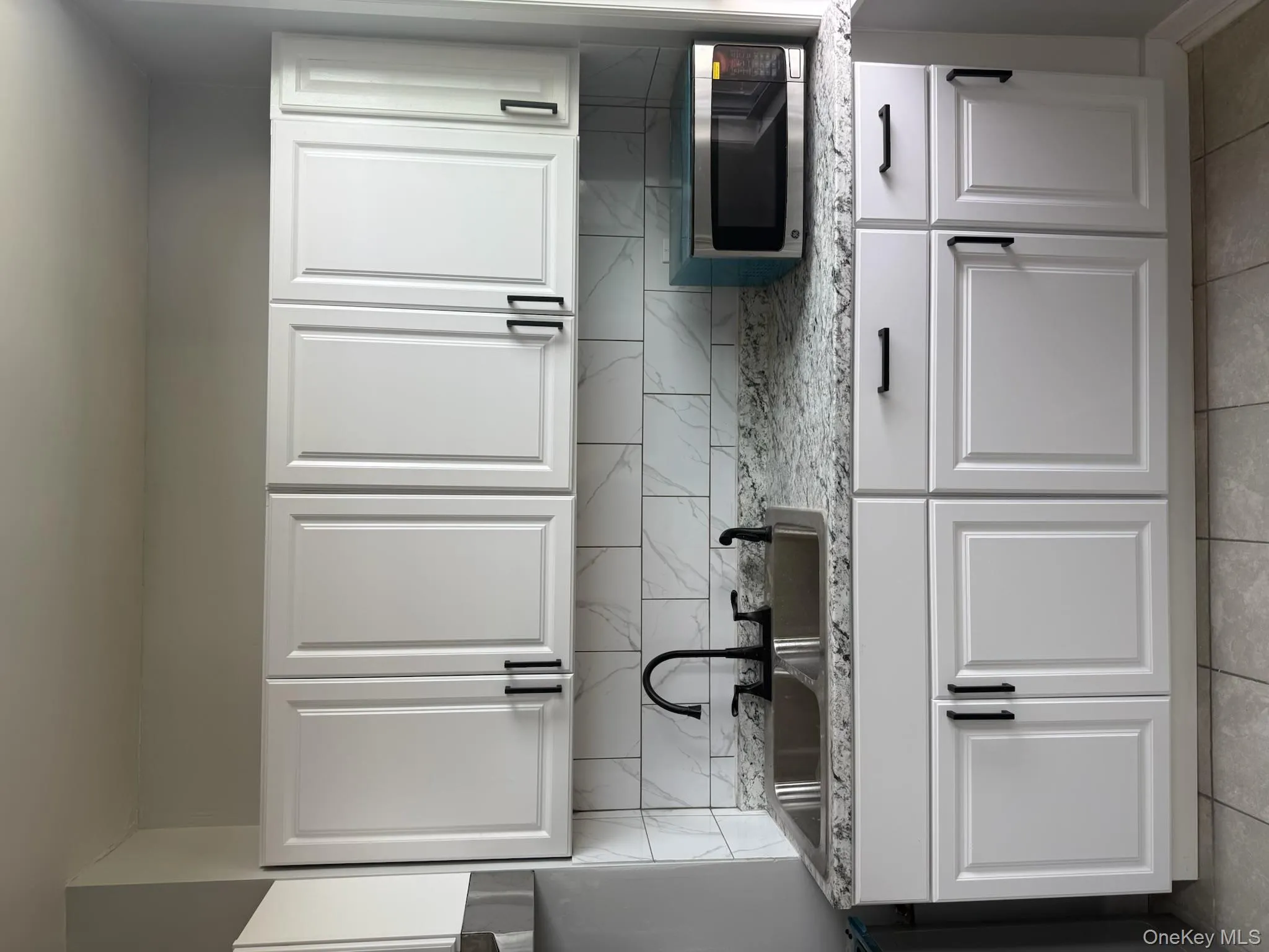 Kitchen with white cabinetry, backsplash, light stone counters, and light tile patterned floors Kitchen with white cabinetry, backsplash, light stone counters, and light tile patterned floors