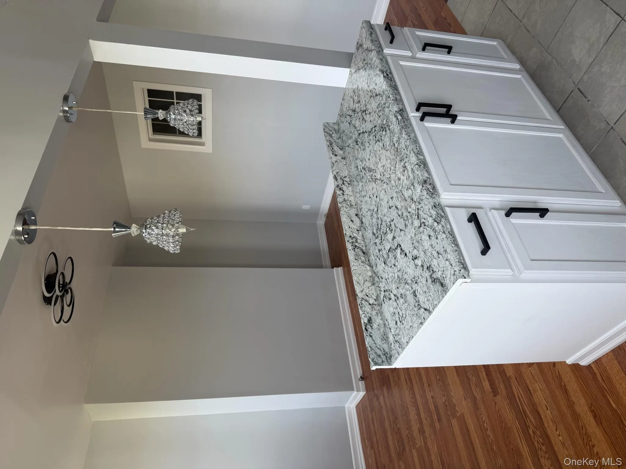 Kitchen with white cabinets, decorative light fixtures, light stone counters, and a kitchen island Kitchen with white cabinets, decorative light fixtures, light stone counters, and a kitchen island