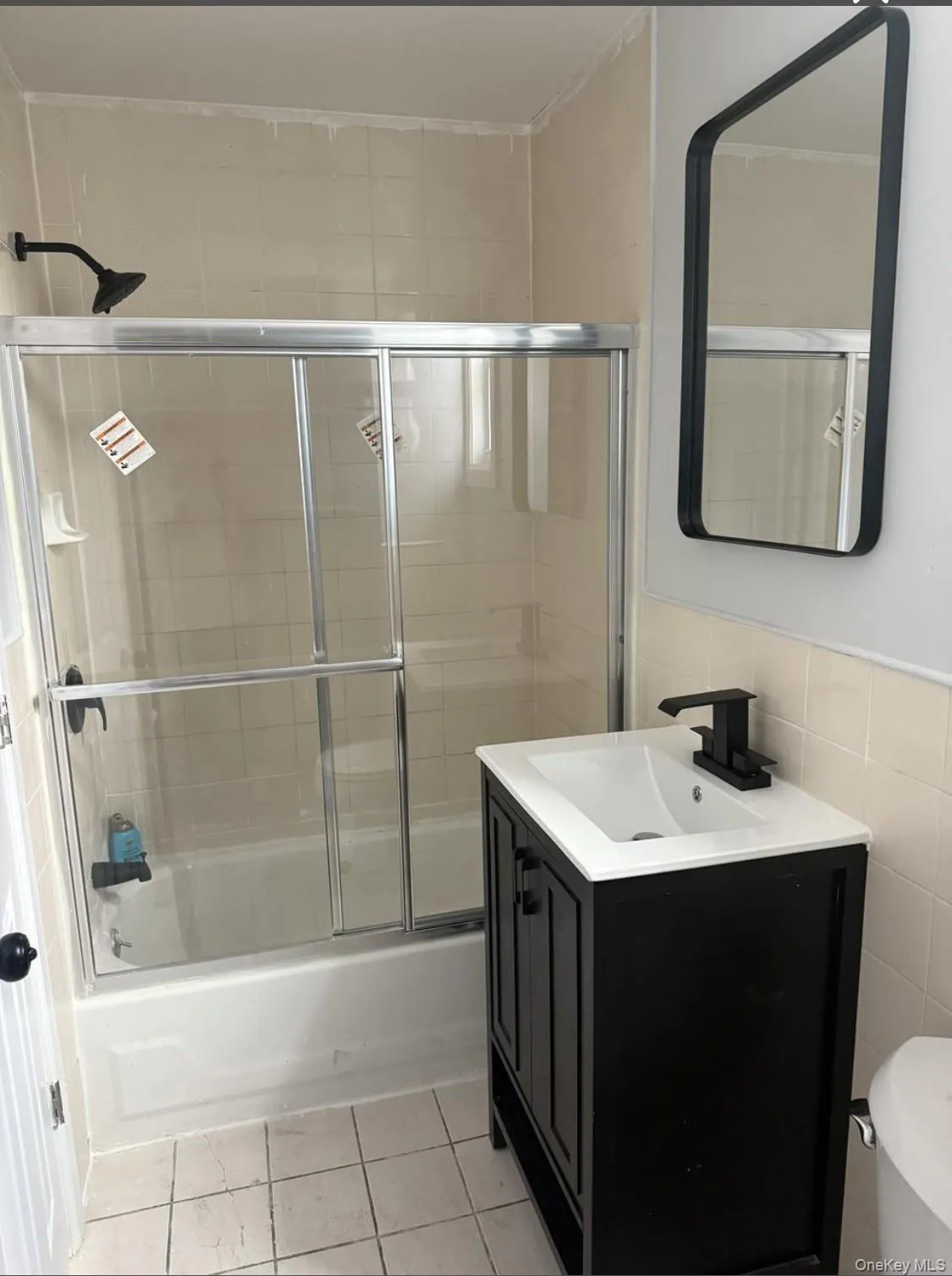 Full bathroom featuring bath / shower combo with glass door, vanity, tile walls, and light tile patterned floors Full bathroom featuring bath / shower combo with glass door, vanity, tile walls, and light tile patterned floors