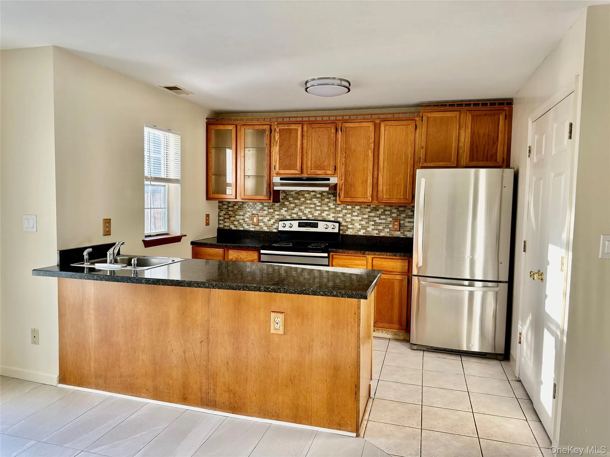 Kitchen with sink, decorative backsplash, dark stone countertops, kitchen peninsula, and stainless steel appliances Kitchen with sink, decorative backsplash, dark stone countertops, kitchen peninsula, and stainless steel appliances
