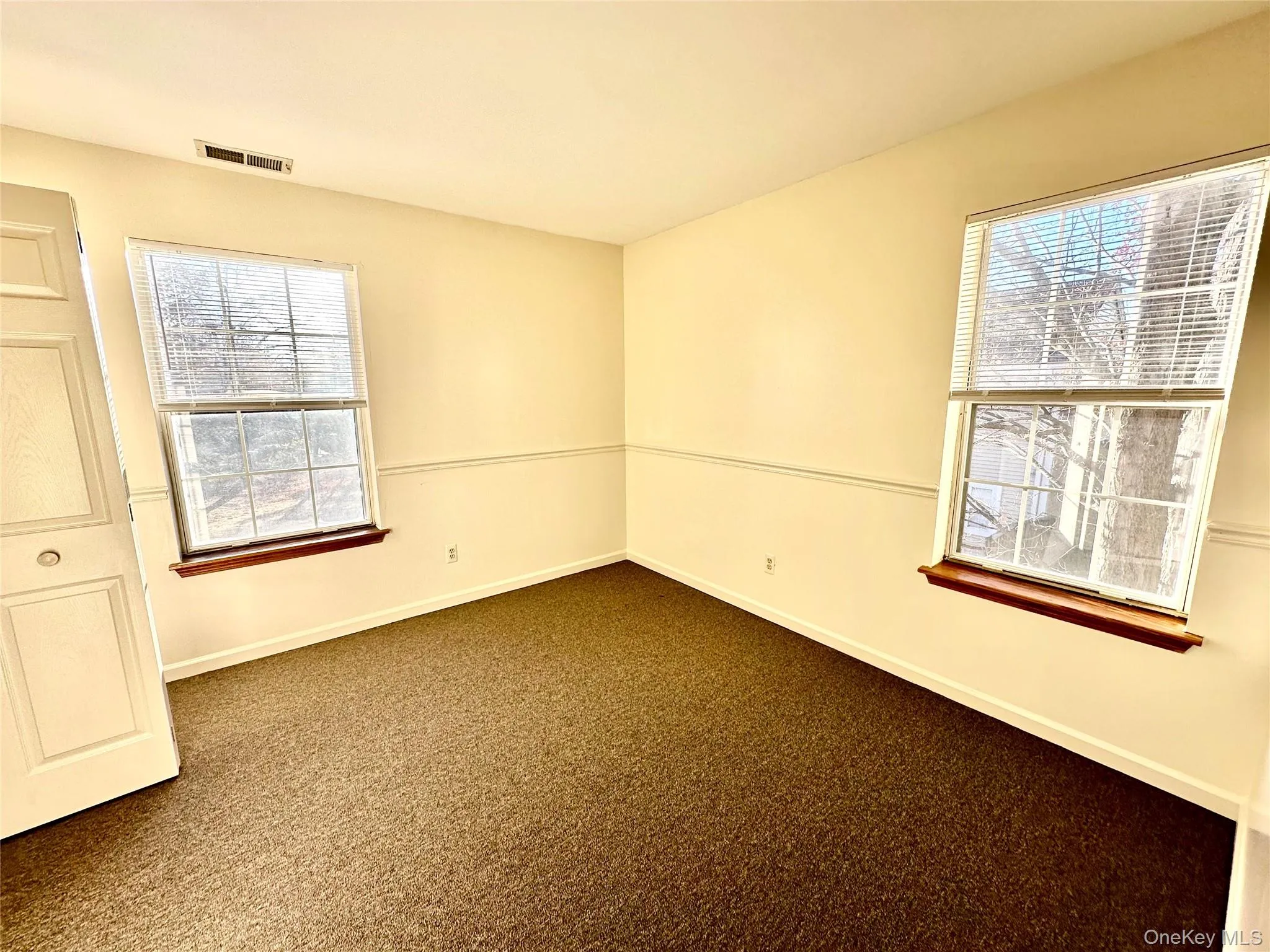 Second bedroom with double closet featuring dark colored carpet and a wealth of natural light Second bedroom with double closet featuring dark colored carpet and a wealth of natural light