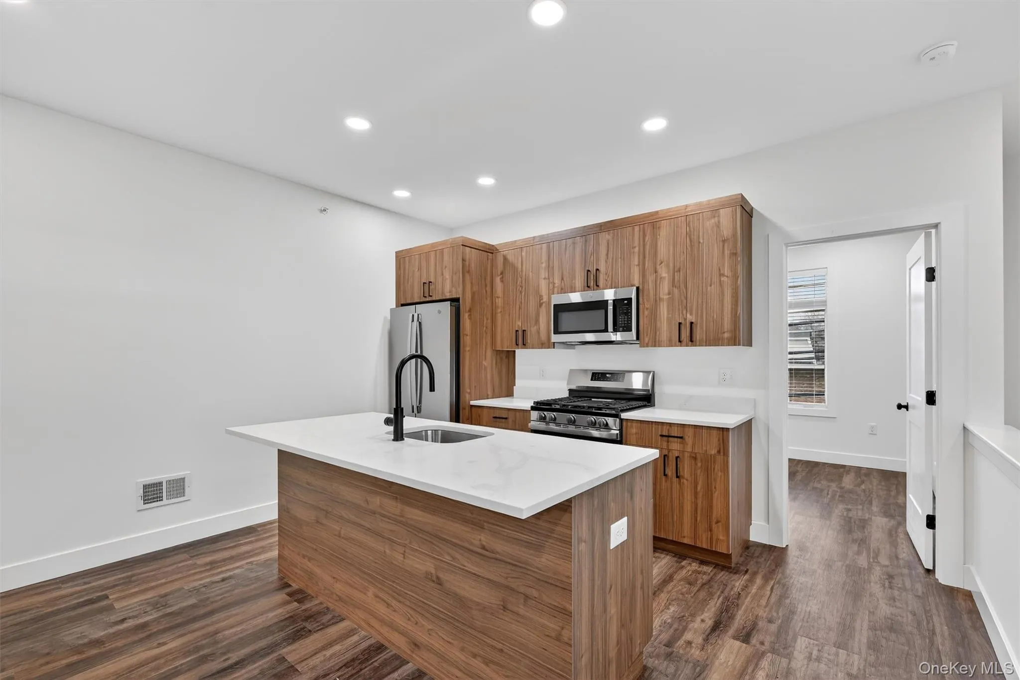 Kitchen featuring brown cabinets, an island with sink, stainless steel appliances, dark wood-type flooring, and light stone counters Kitchen featuring brown cabinets, an island with sink, stainless steel appliances, dark wood-type flooring, and light stone counters