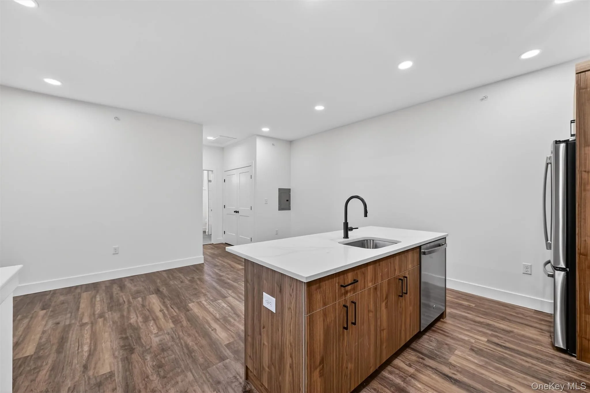 Kitchen with brown cabinetry, dark wood-style flooring, recessed lighting, a center island with sink, and light stone counters Kitchen with brown cabinetry, dark wood-style flooring, recessed lighting, a center island with sink, and light stone counters