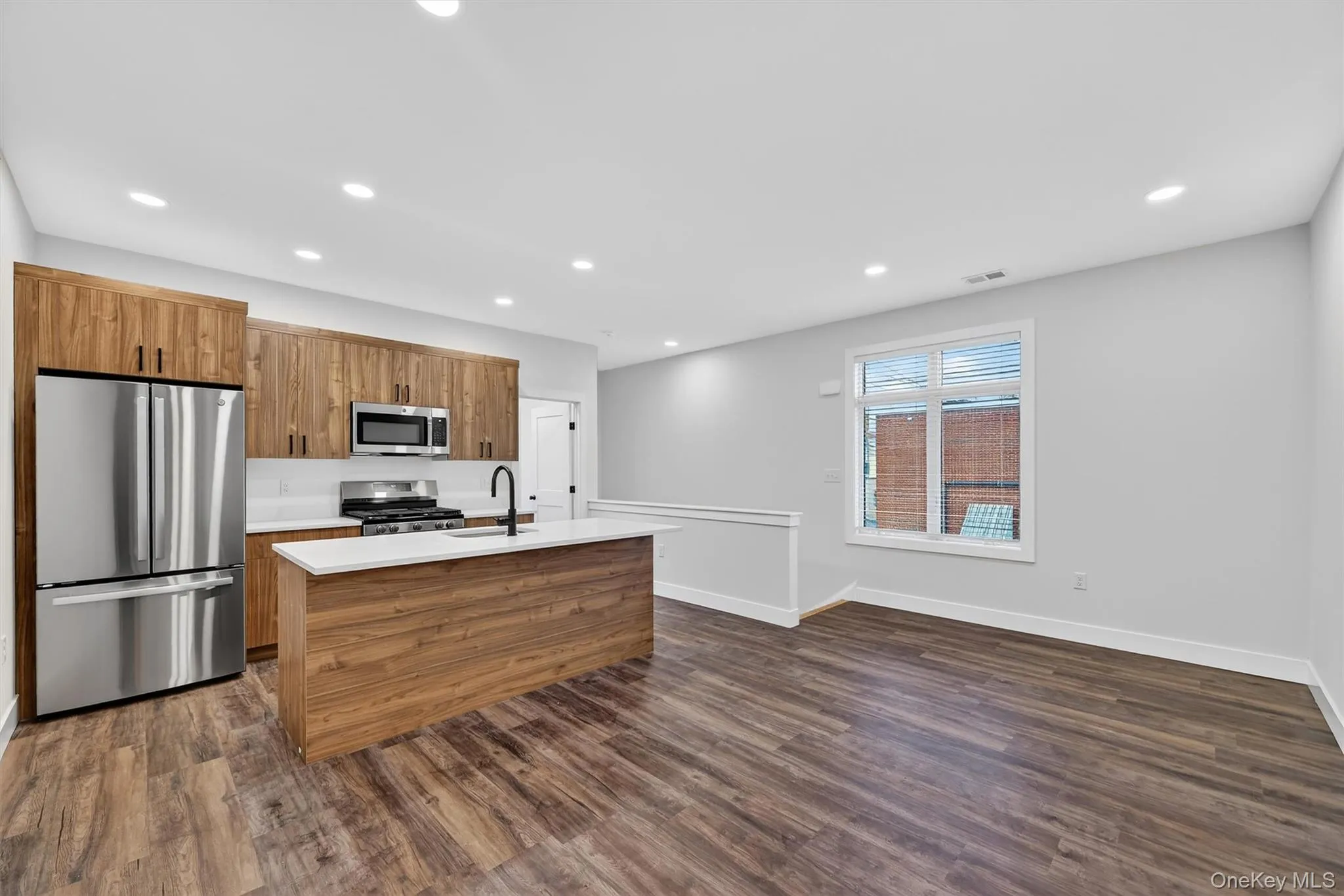 Kitchen with stainless steel appliances, brown cabinetry, dark wood-type flooring, a center island with sink, and recessed lighting Kitchen with stainless steel appliances, brown cabinetry, dark wood-type flooring, a center island with sink, and recessed lighting