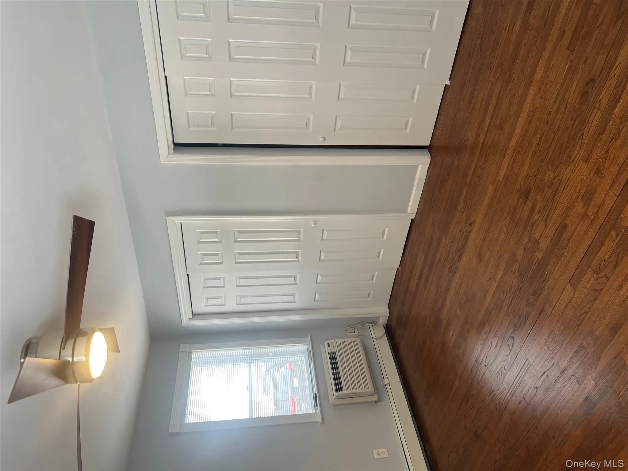 Unfurnished bedroom with multiple closets, a baseboard radiator, dark wood finished floors, ceiling fan, and a wall mounted AC Unfurnished bedroom with multiple closets, a baseboard radiator, dark wood finished floors, ceiling fan, and a wall mounted AC