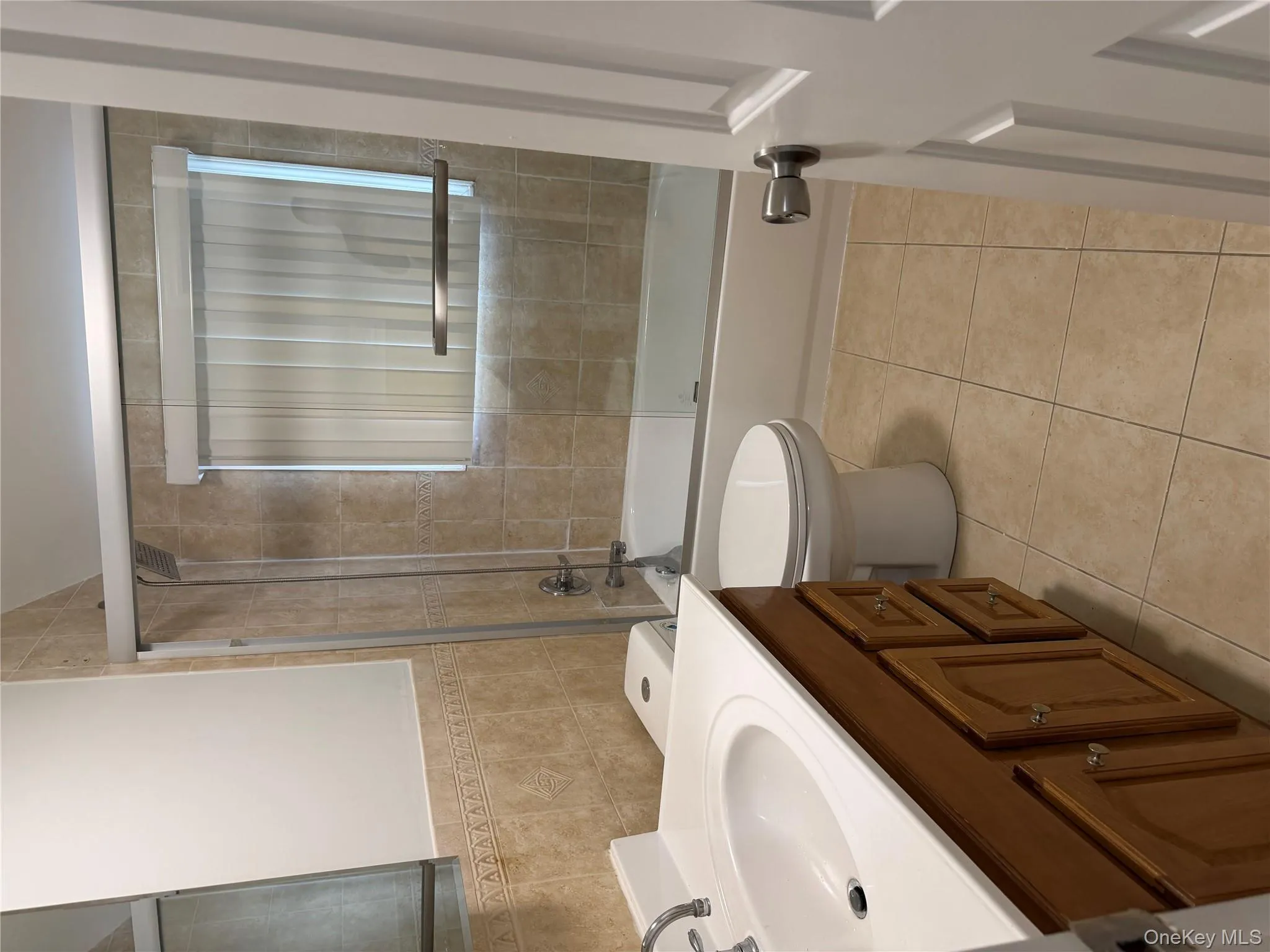 Bathroom featuring bath / shower combo with glass door, tile walls, vanity, light tile patterned flooring, and wainscoting Bathroom featuring bath / shower combo with glass door, tile walls, vanity, light tile patterned flooring, and wainscoting