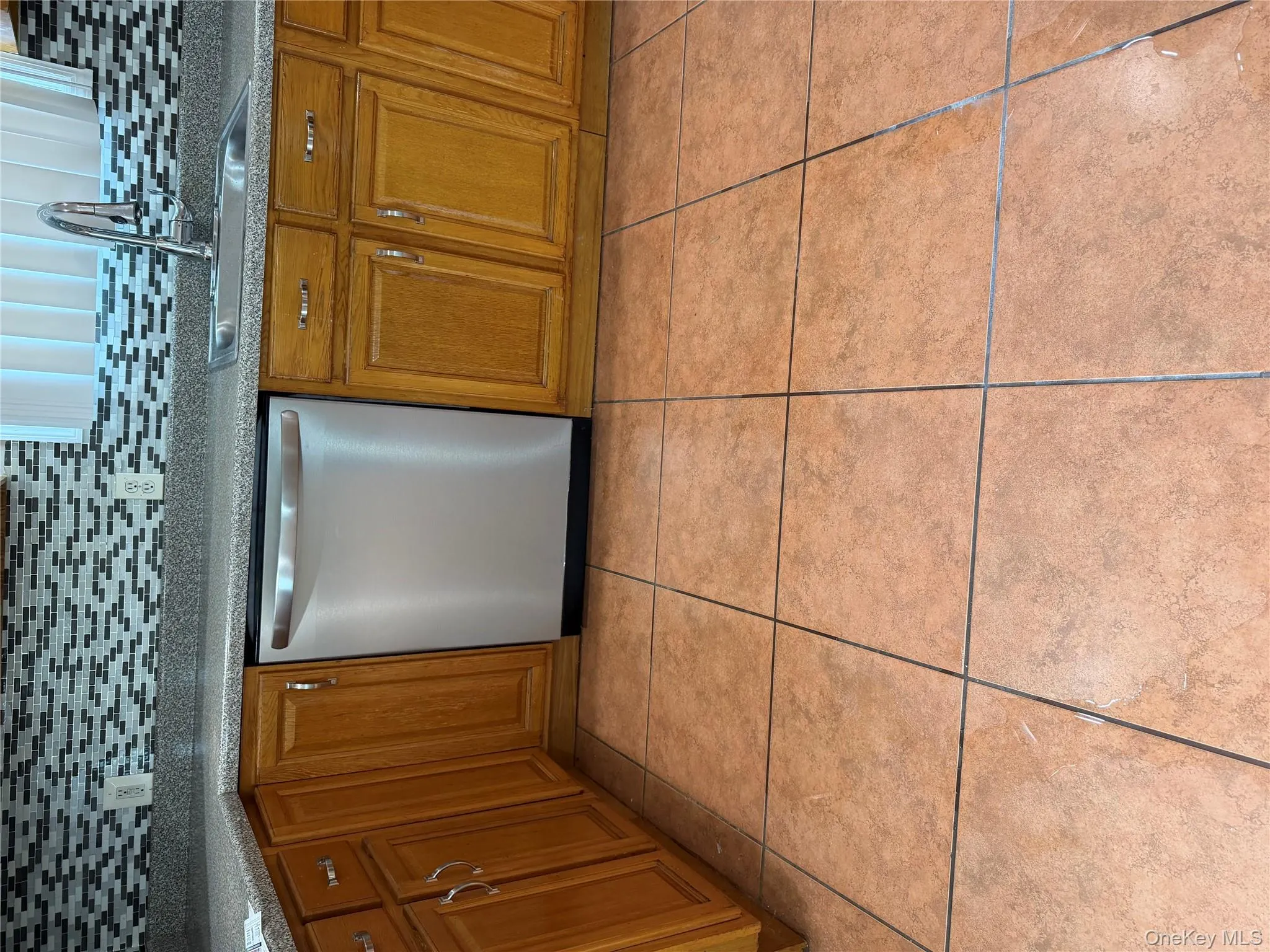 Kitchen featuring dishwasher, brown cabinets, light tile patterned flooring, and tasteful backsplash Kitchen featuring dishwasher, brown cabinets, light tile patterned flooring, and tasteful backsplash