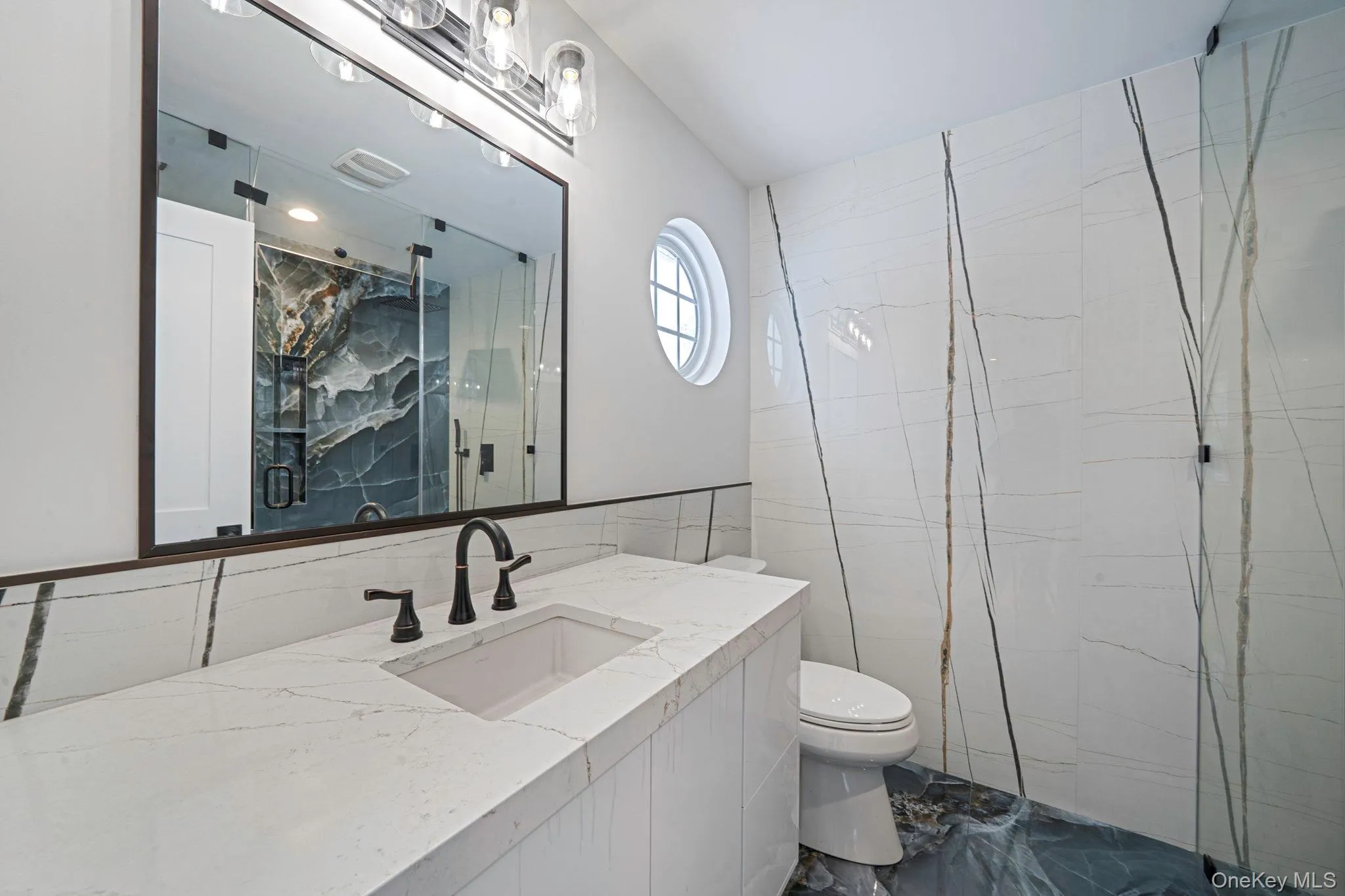 Full bath with tile walls, vanity, a marble finish shower, and dark marble finish floors Full bath with tile walls, vanity, a marble finish shower, and dark marble finish floors