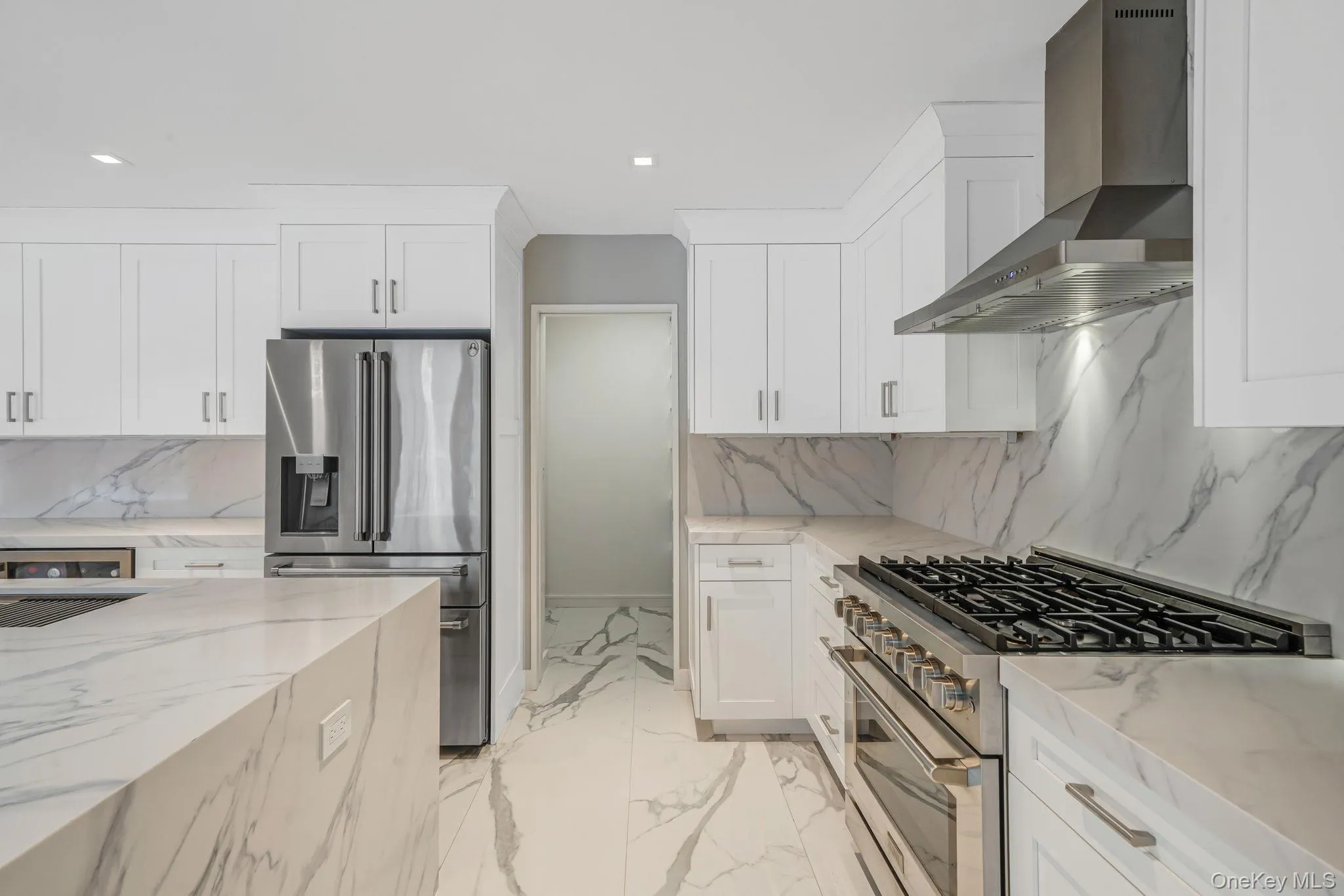 Kitchen featuring stainless steel appliances, light stone countertops, tasteful backsplash, wall chimney range hood, and white cabinetry Kitchen featuring stainless steel appliances, light stone countertops, tasteful backsplash, wall chimney range hood, and white cabinetry