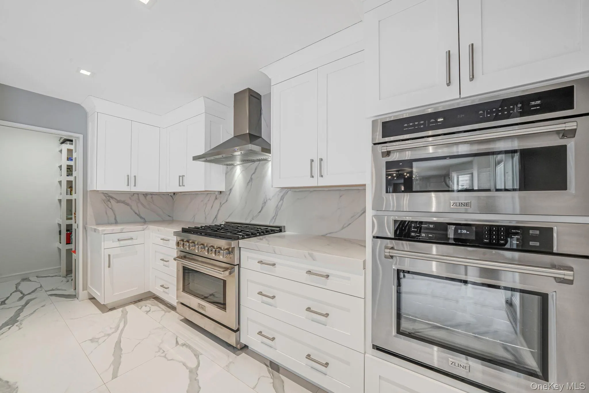 Kitchen featuring appliances with stainless steel finishes, light marble finish floors, white cabinets, wall chimney range hood, and light stone countertops Kitchen featuring appliances with stainless steel finishes, light marble finish floors, white cabinets, wall chimney range hood, and light stone countertops