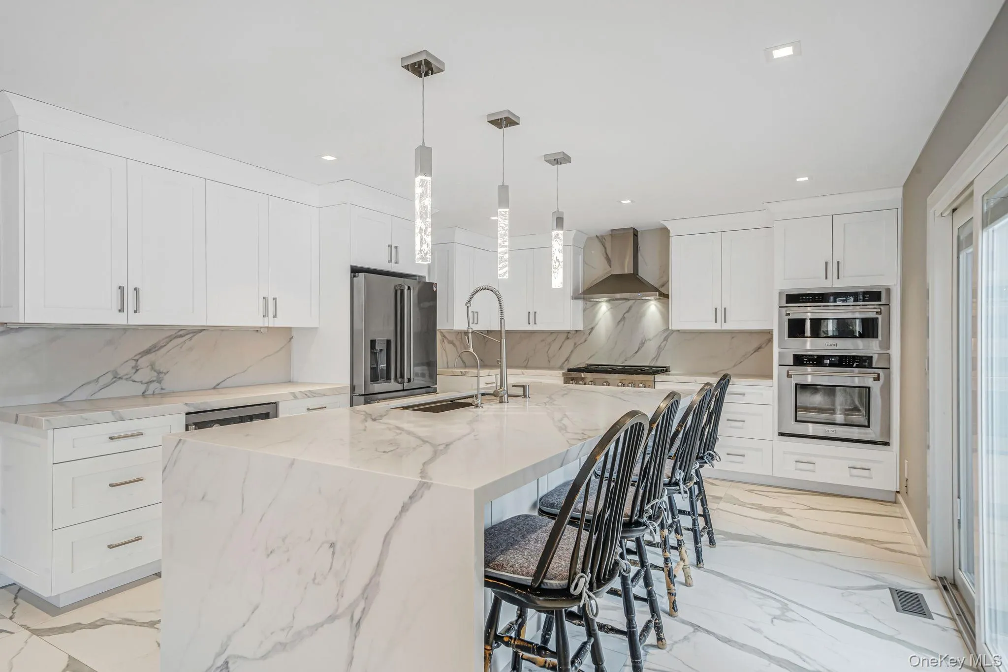 Kitchen featuring a breakfast bar area, decorative light fixtures, light marble finish floors, white cabinetry, and recessed lighting Kitchen featuring a breakfast bar area, decorative light fixtures, light marble finish floors, white cabinetry, and recessed lighting