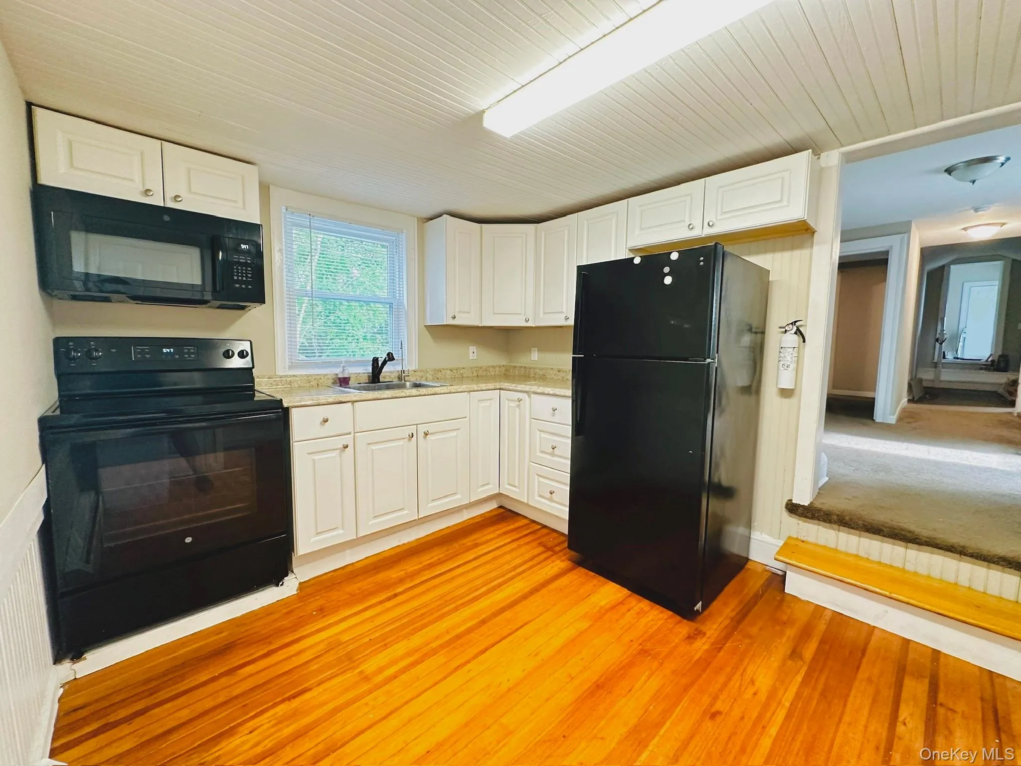 Kitchen with black appliances, white cabinetry, light wood-type flooring, and wood ceiling Kitchen with black appliances, white cabinetry, light wood-type flooring, and wood ceiling