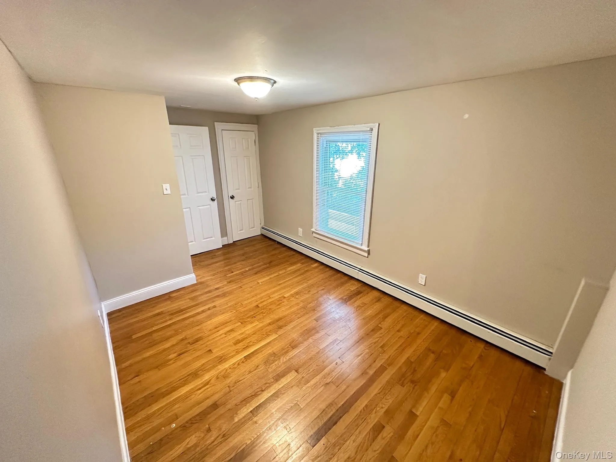 Unfurnished bedroom with a baseboard heating unit and light wood-style floors Unfurnished bedroom with a baseboard heating unit and light wood-style floors