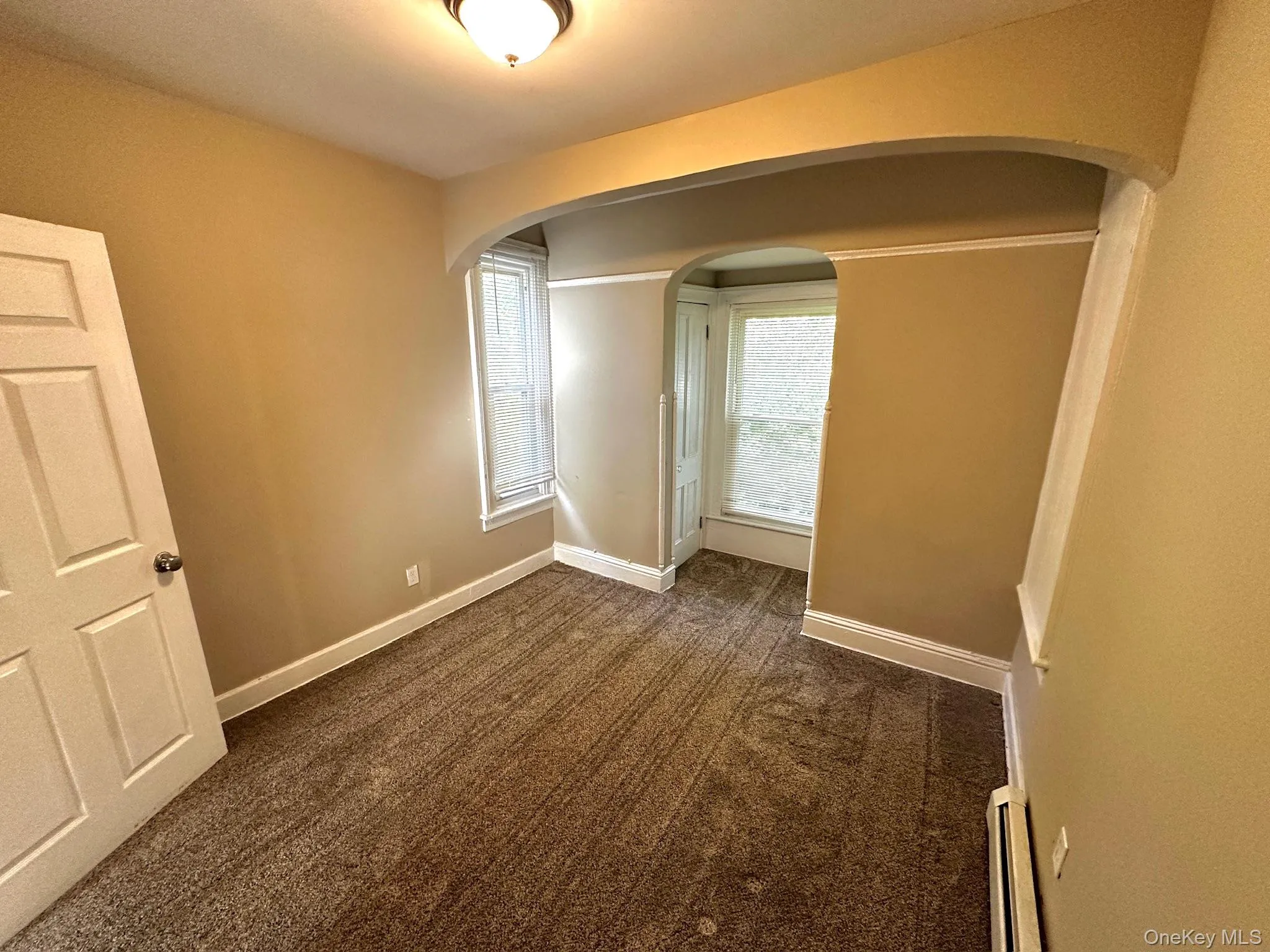 Spare room with arched walkways, dark carpet, and a baseboard radiator Spare room with arched walkways, dark carpet, and a baseboard radiator