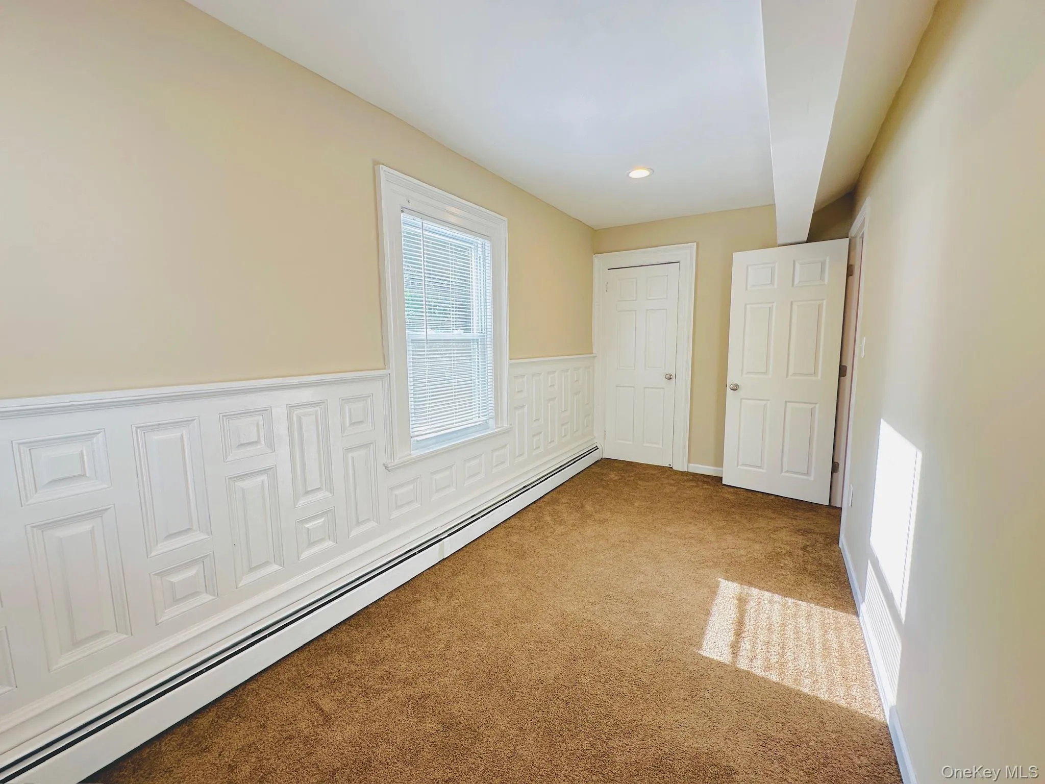 Carpeted empty room with a baseboard heating unit, recessed lighting, wainscoting, and a decorative wall Carpeted empty room with a baseboard heating unit, recessed lighting, wainscoting, and a decorative wall