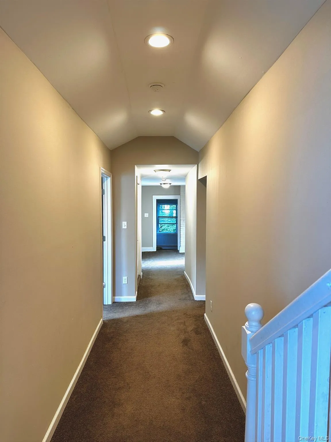 Hallway with dark colored carpet, vaulted ceiling, and recessed lighting Hallway with dark colored carpet, vaulted ceiling, and recessed lighting