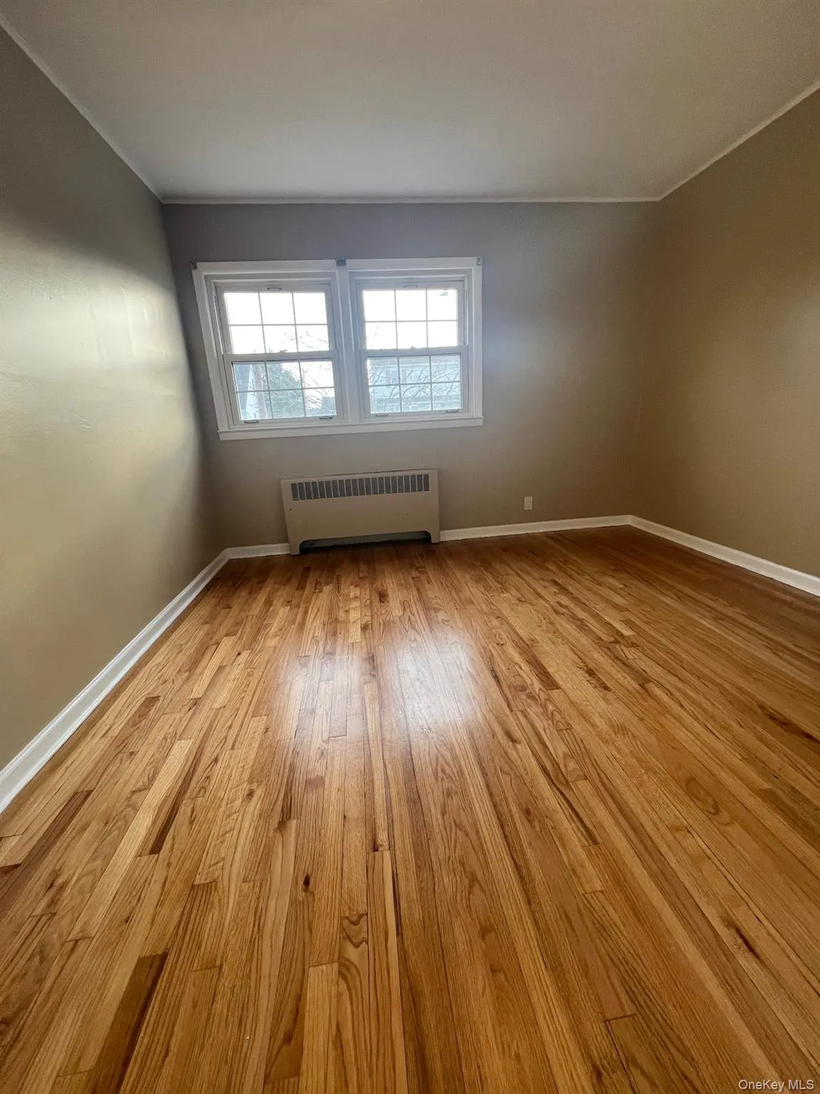 Empty room with radiator heating unit, light wood-style floors, and ornamental molding Empty room with radiator heating unit, light wood-style floors, and ornamental molding