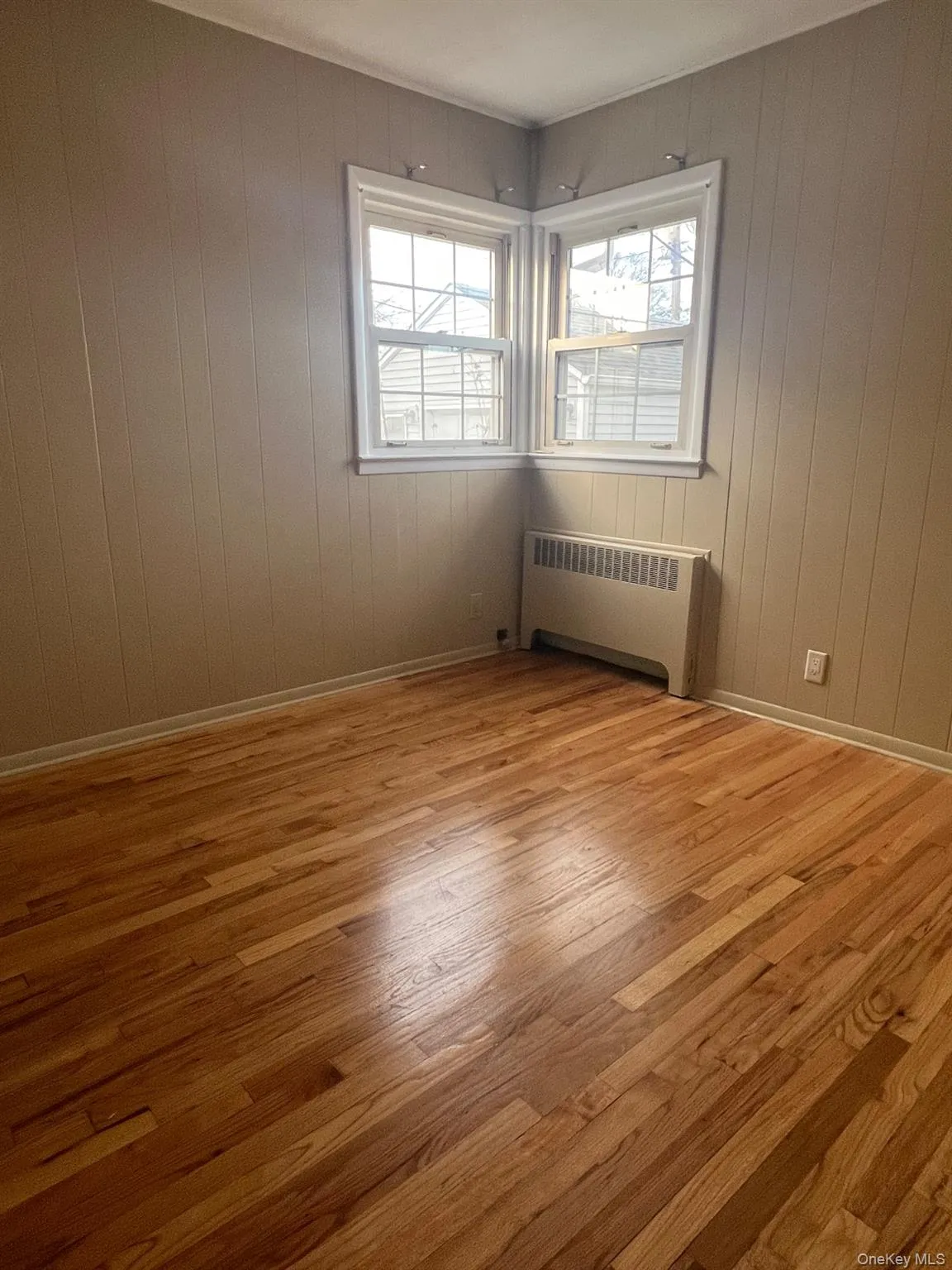 Empty room featuring radiator heating unit, light wood-style flooring, and wooden walls Empty room featuring radiator heating unit, light wood-style flooring, and wooden walls