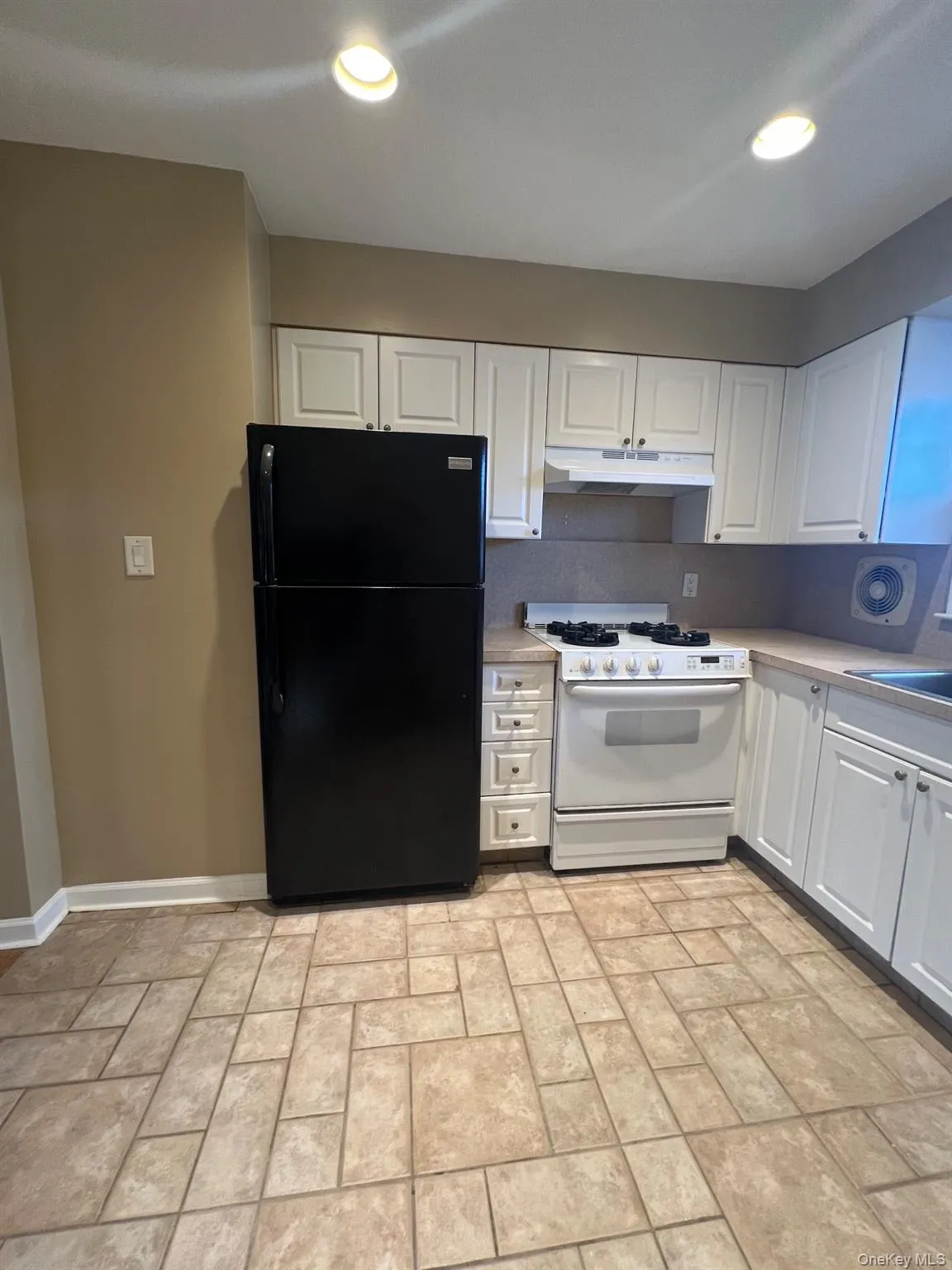 Kitchen with white gas range, freestanding refrigerator, white cabinets, under cabinet range hood, and light countertops Kitchen with white gas range, freestanding refrigerator, white cabinets, under cabinet range hood, and light countertops
