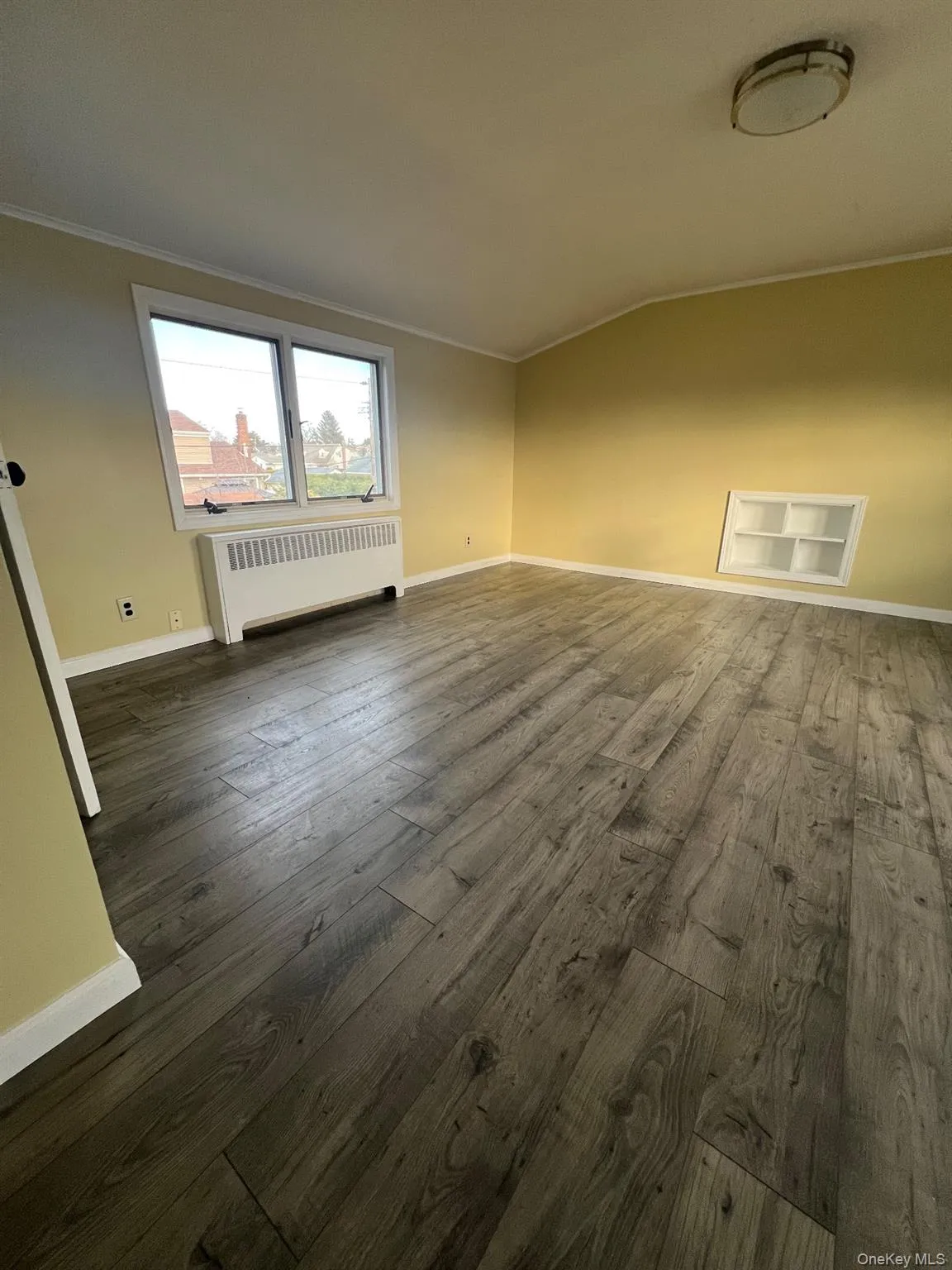 Empty room featuring radiator, dark wood finished floors, crown molding, and vaulted ceiling Empty room featuring radiator, dark wood finished floors, crown molding, and vaulted ceiling