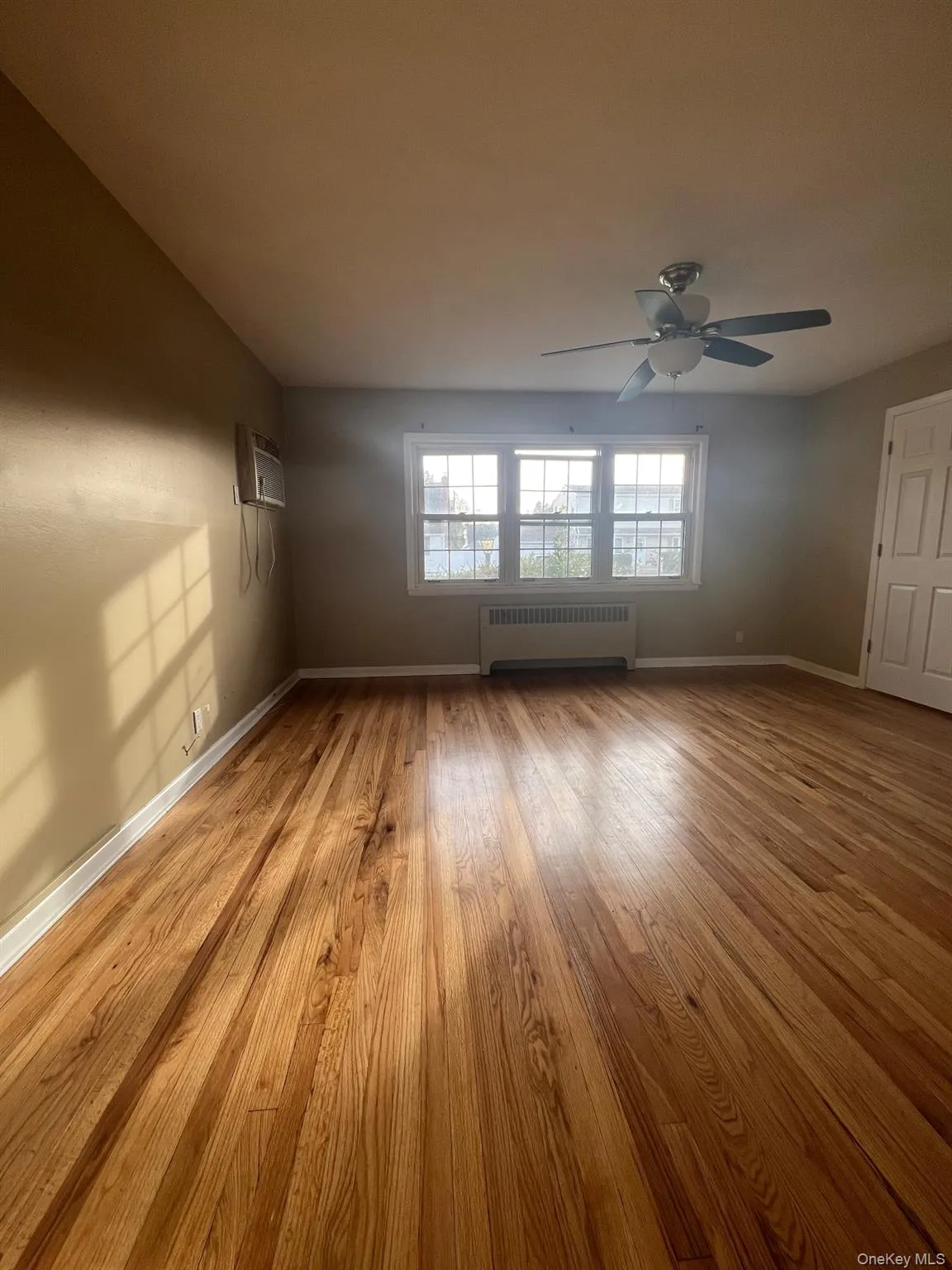 Spare room featuring radiator heating unit, light wood-style flooring, and a wall unit AC Spare room featuring radiator heating unit, light wood-style flooring, and a wall unit AC