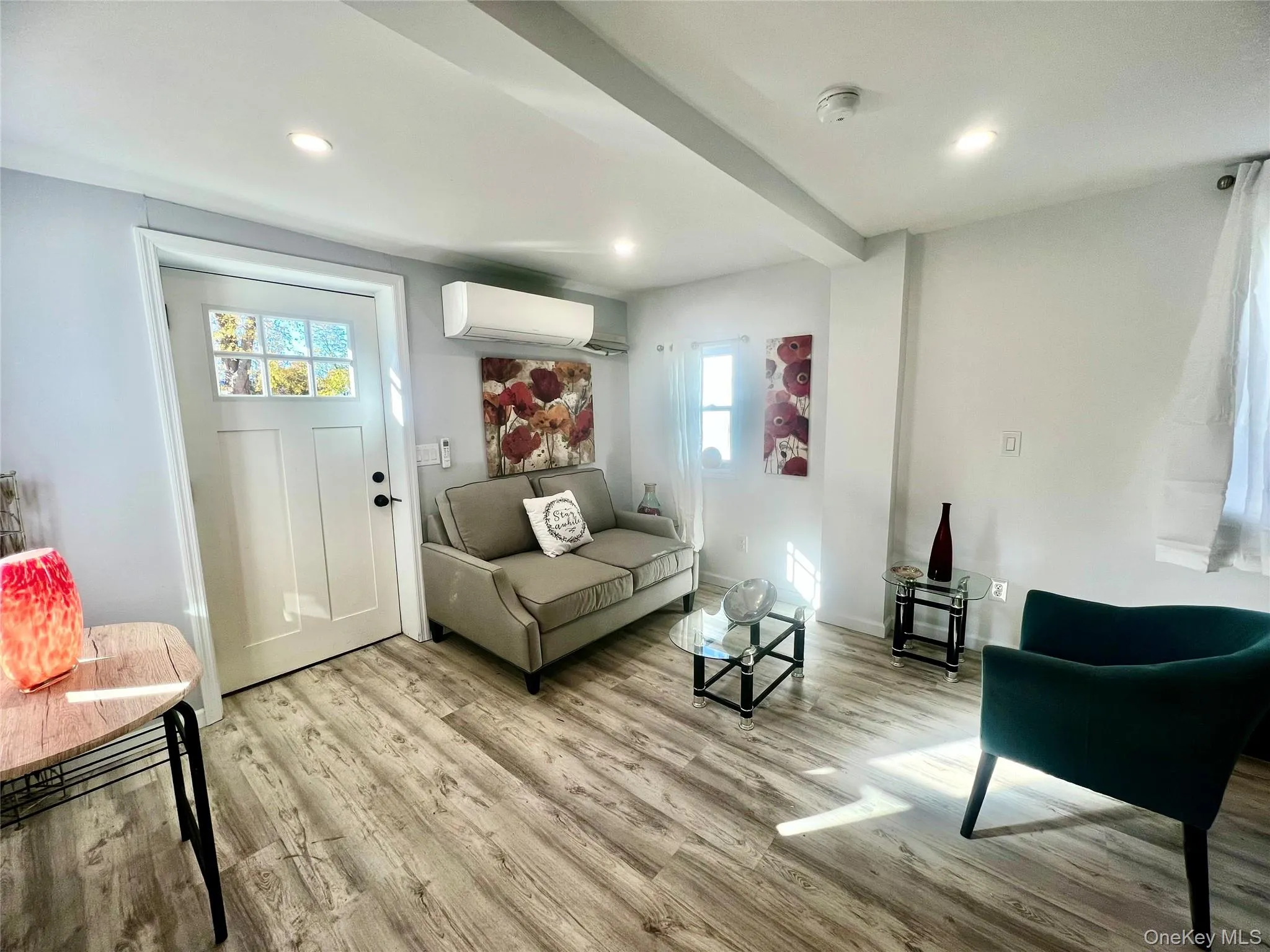 Living room with light wood-style floors, beam ceiling, recessed lighting, and an AC wall unit Living room with light wood-style floors, beam ceiling, recessed lighting, and an AC wall unit