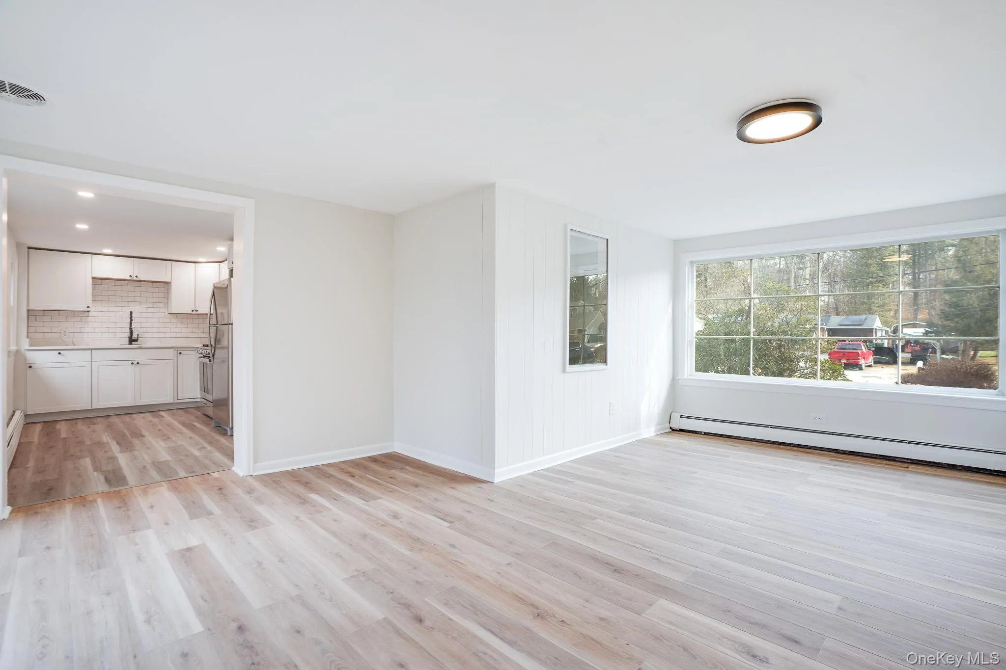 Unfurnished living room featuring light wood-style floors, a baseboard heating unit, and recessed lighting Unfurnished living room featuring light wood-style floors, a baseboard heating unit, and recessed lighting