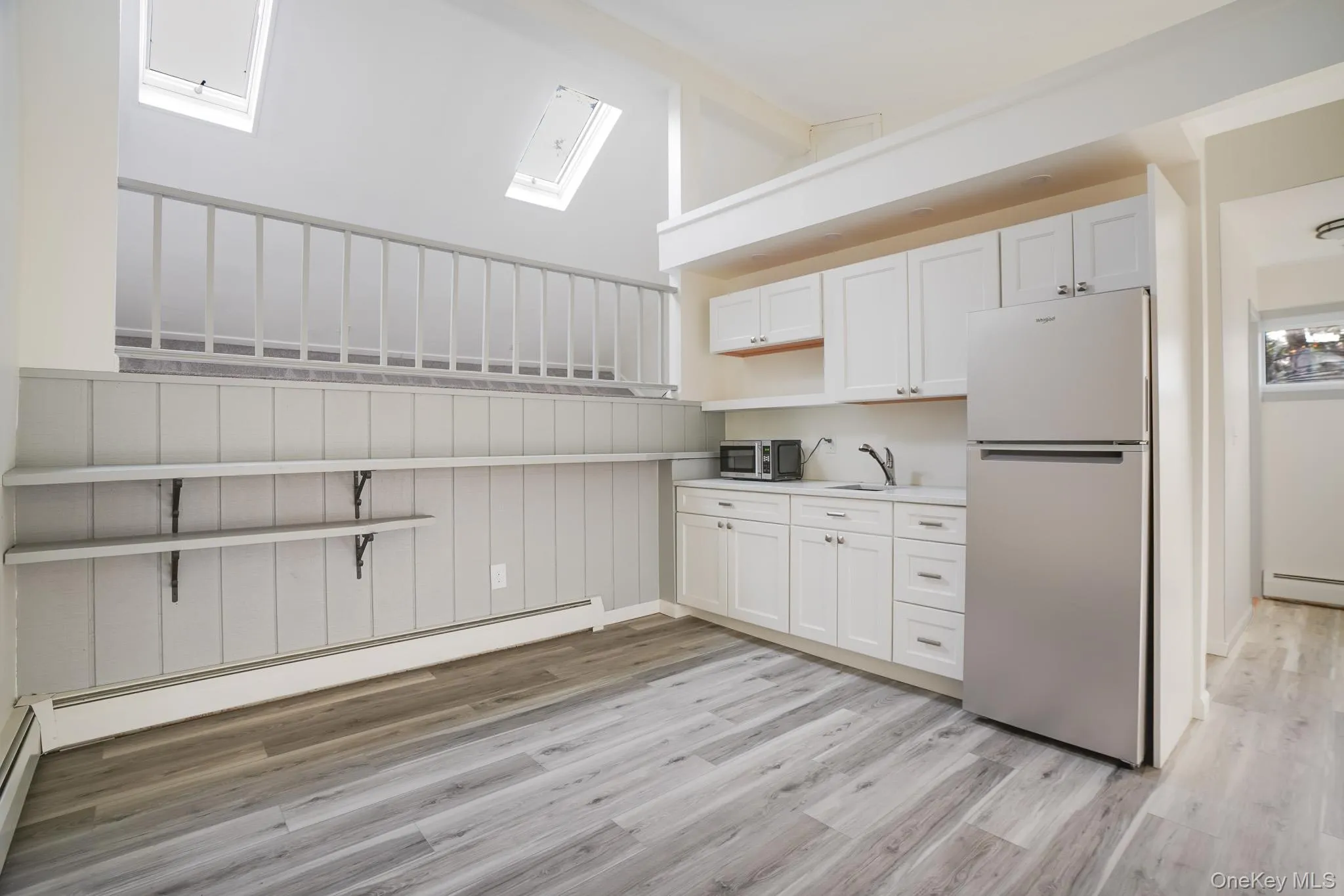 Kitchen featuring open shelves, freestanding refrigerator, white cabinets, light countertops, and a baseboard heating unit Kitchen featuring open shelves, freestanding refrigerator, white cabinets, light countertops, and a baseboard heating unit