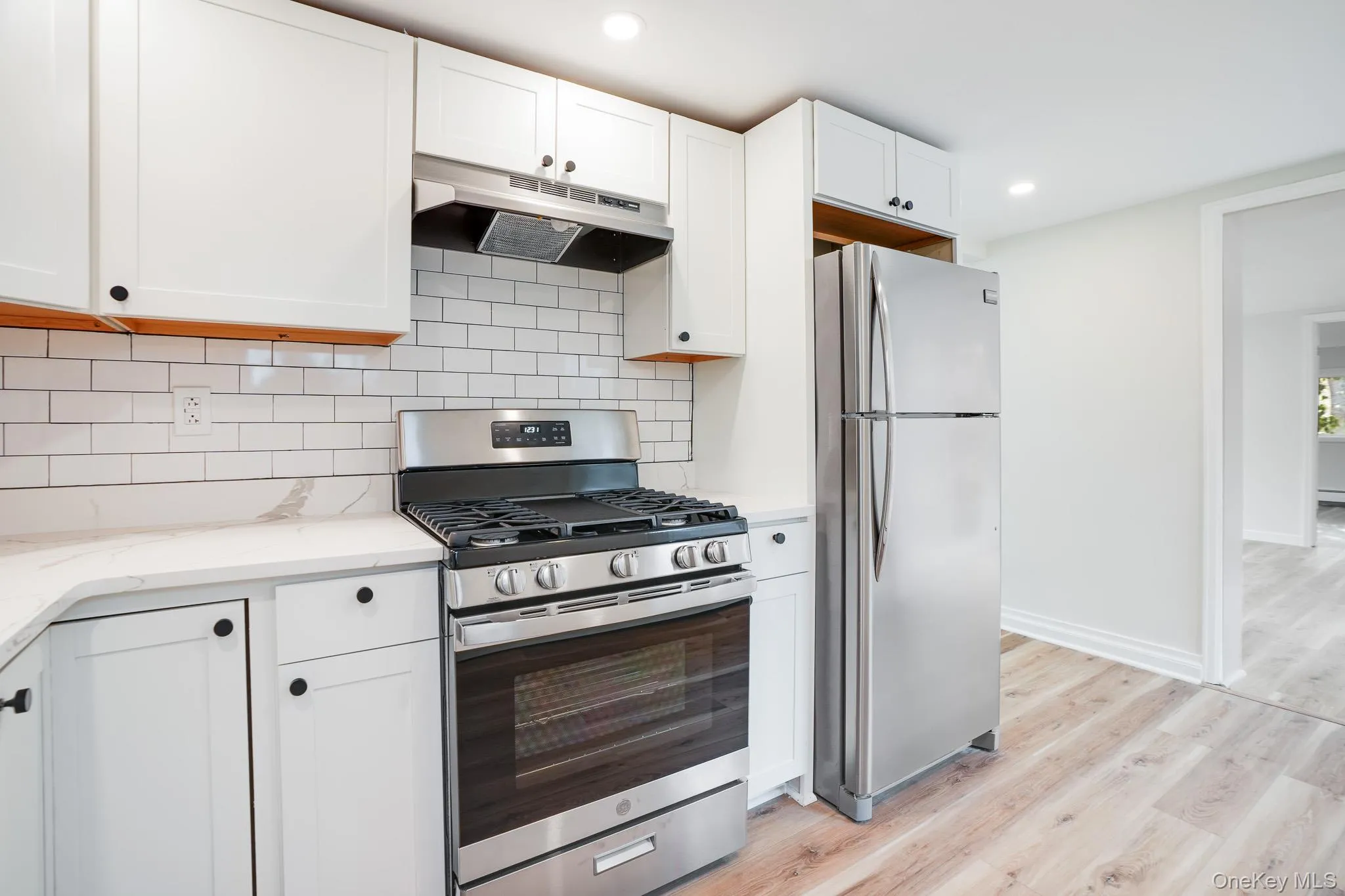 Kitchen featuring stainless steel appliances, under cabinet range hood, tasteful backsplash, light wood-type flooring, and white cabinets Kitchen featuring stainless steel appliances, under cabinet range hood, tasteful backsplash, light wood-type flooring, and white cabinets