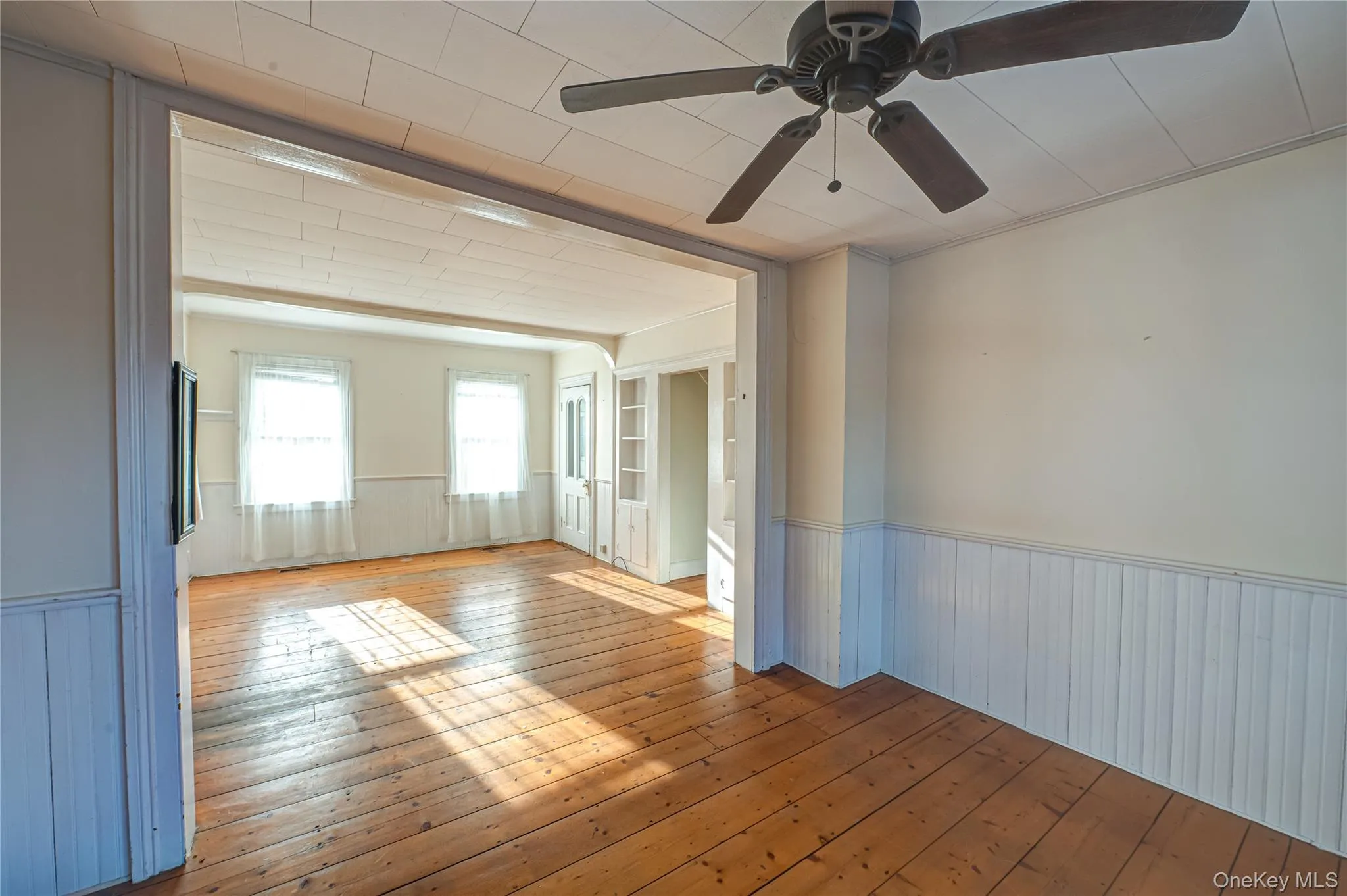 Spare room featuring wainscoting, light wood-style flooring, and a ceiling fan Spare room featuring wainscoting, light wood-style flooring, and a ceiling fan