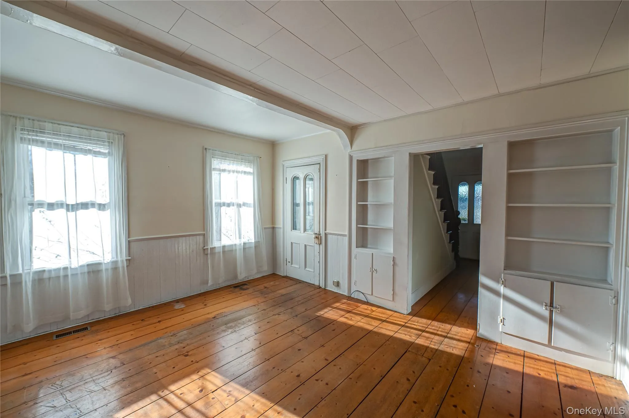 Unfurnished room featuring light wood finished floors, a wainscoted wall, and built in shelves Unfurnished room featuring light wood finished floors, a wainscoted wall, and built in shelves