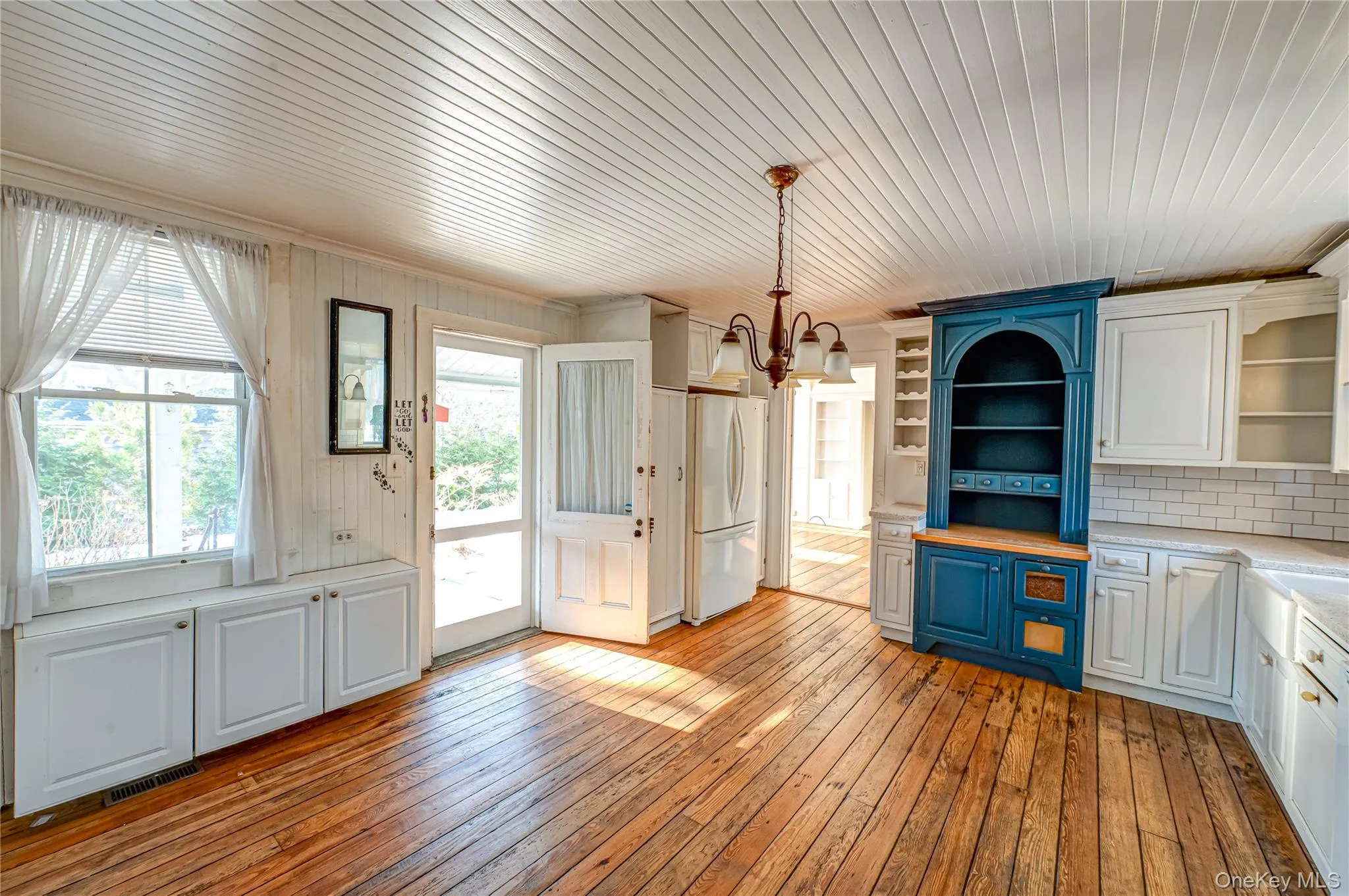 Kitchen with white cabinets, light wood-style floors, wood ceiling, a chandelier, and hanging light fixtures Kitchen with white cabinets, light wood-style floors, wood ceiling, a chandelier, and hanging light fixtures