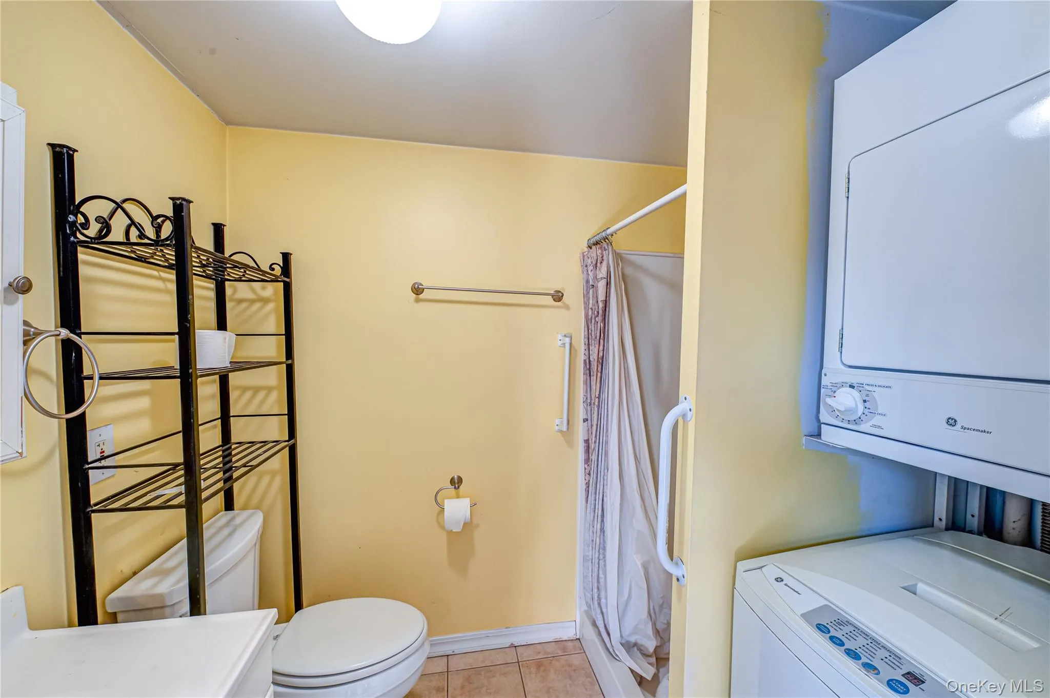 Bathroom with curtained shower, light tile patterned floors, stacked washing machine and dryer, and vanity Bathroom with curtained shower, light tile patterned floors, stacked washing machine and dryer, and vanity