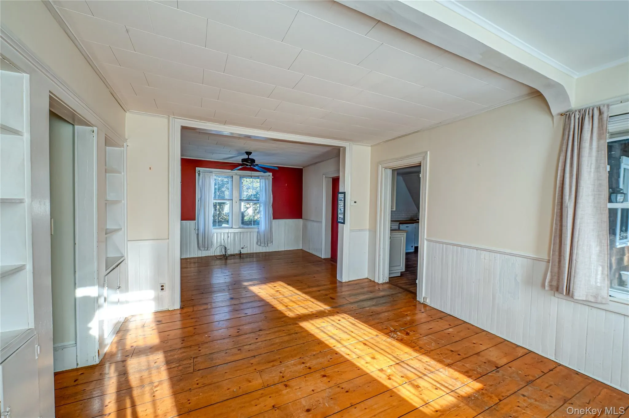 Spare room with wainscoting, wood-type flooring, a ceiling fan, and built in shelves Spare room with wainscoting, wood-type flooring, a ceiling fan, and built in shelves