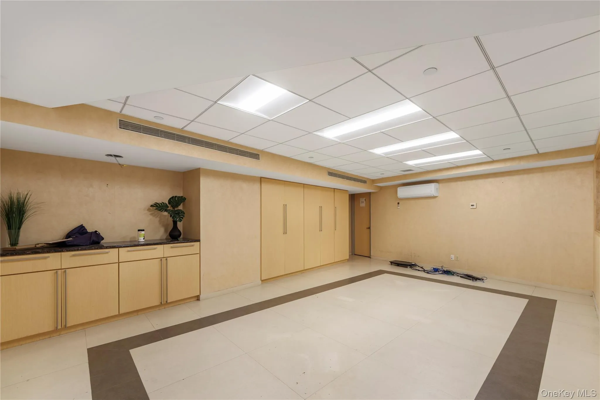 Below grade area with inlaid floor details, an AC wall unit, and a drop ceiling Below grade area with inlaid floor details, an AC wall unit, and a drop ceiling