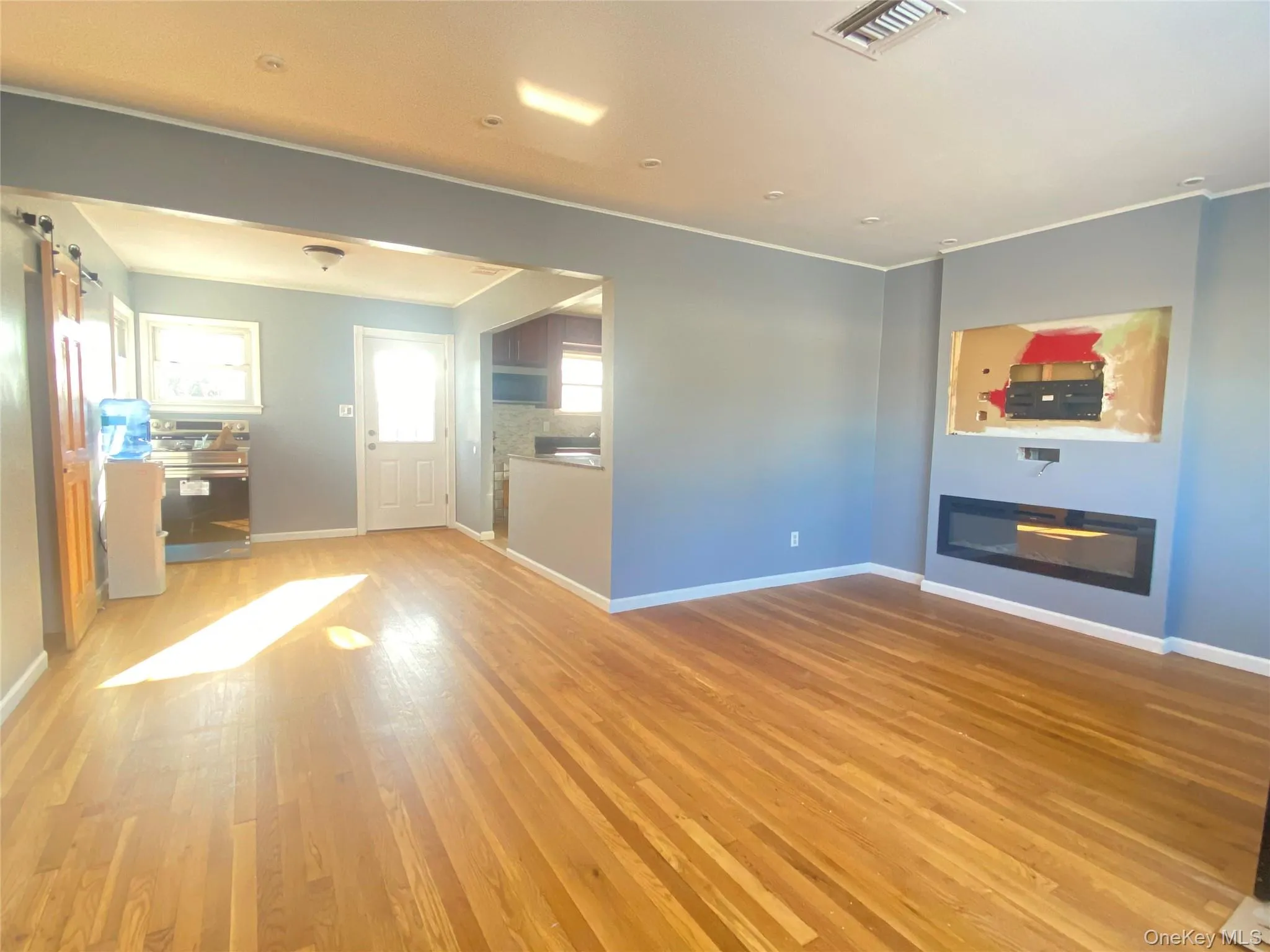 Unfurnished living room featuring a glass covered fireplace, light wood-style flooring, and a barn door Unfurnished living room featuring a glass covered fireplace, light wood-style flooring, and a barn door