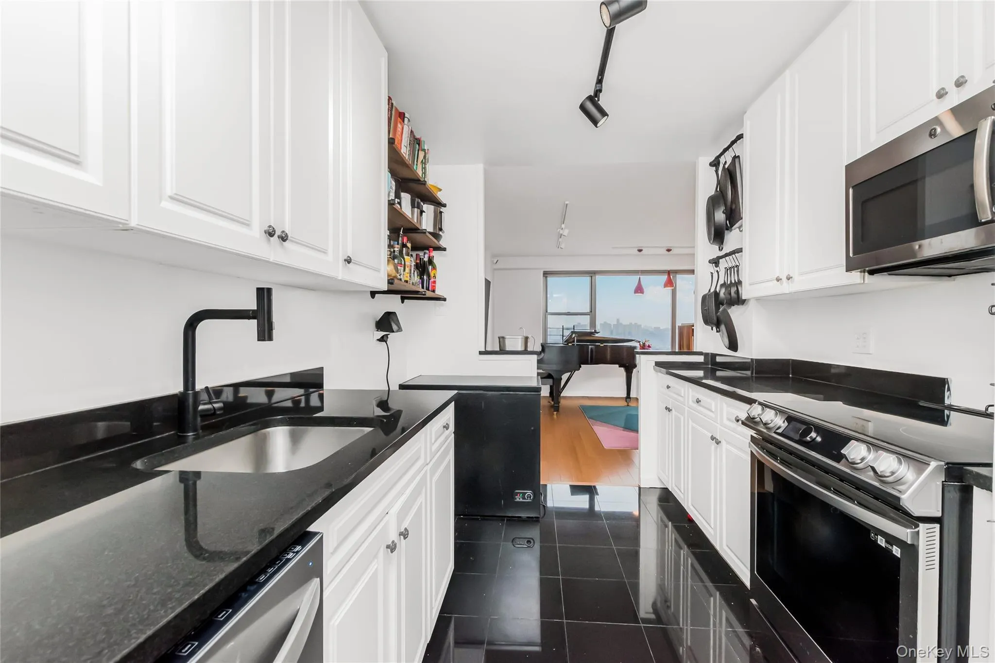 Kitchen with stainless steel appliances, white cabinetry, open shelves, dark stone counters, and rail lighting Kitchen with stainless steel appliances, white cabinetry, open shelves, dark stone counters, and rail lighting