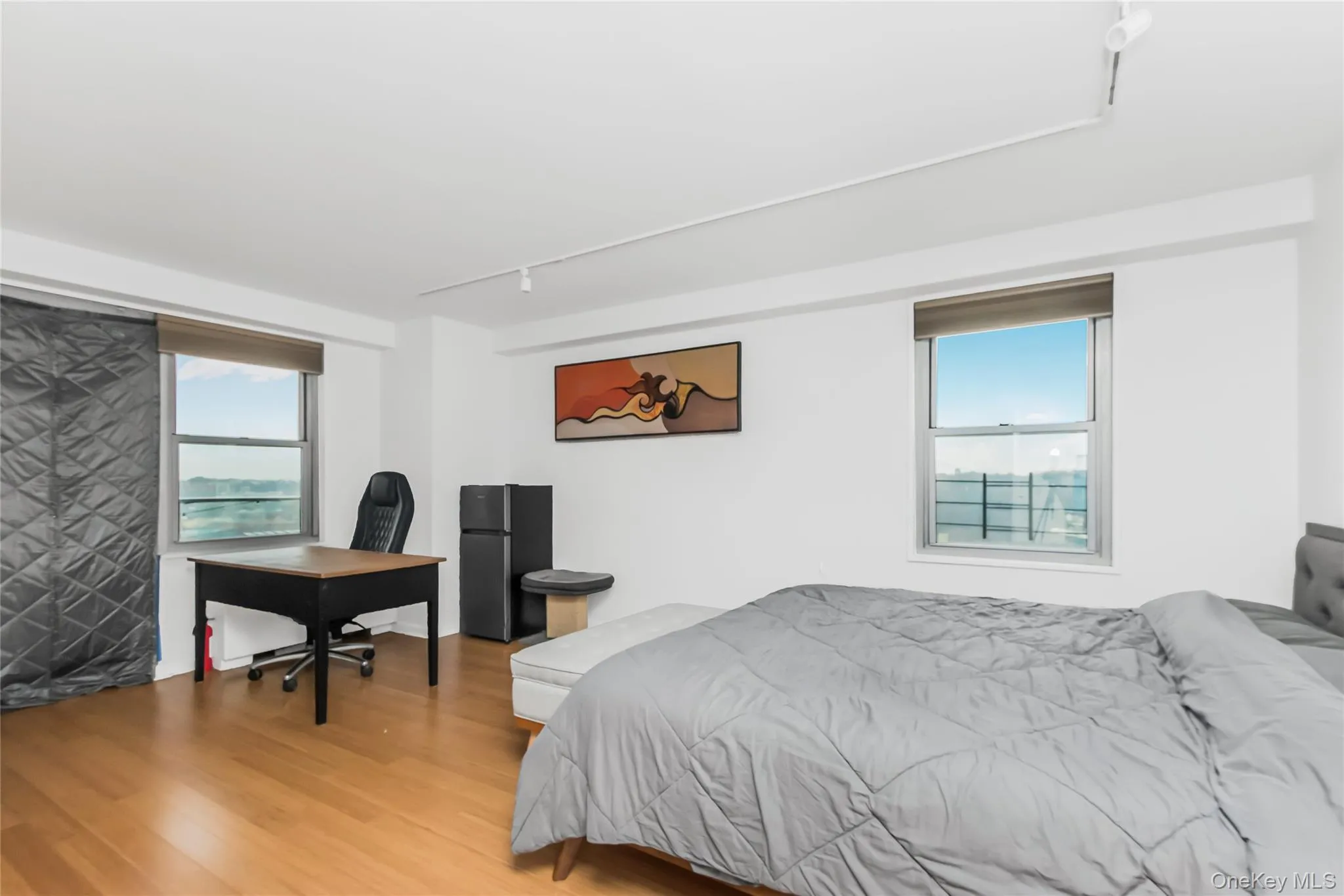 Bedroom featuring track lighting, wood finished floors, freestanding refrigerator, and a desk Bedroom featuring track lighting, wood finished floors, freestanding refrigerator, and a desk