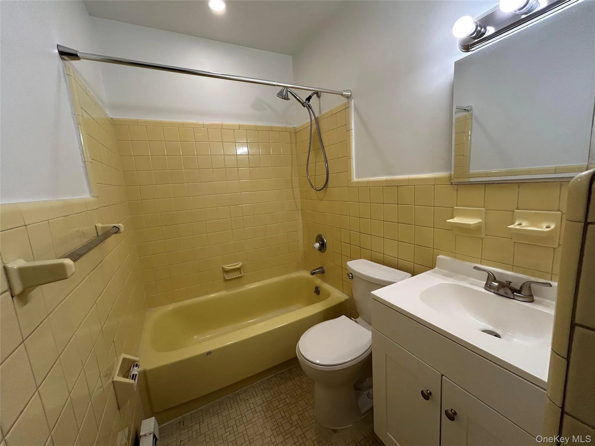 Full bathroom featuring tile walls, vanity, shower / washtub combination, a wainscoted wall, and a baseboard heating unit Full bathroom featuring tile walls, vanity, shower / washtub combination, a wainscoted wall, and a baseboard heating unit