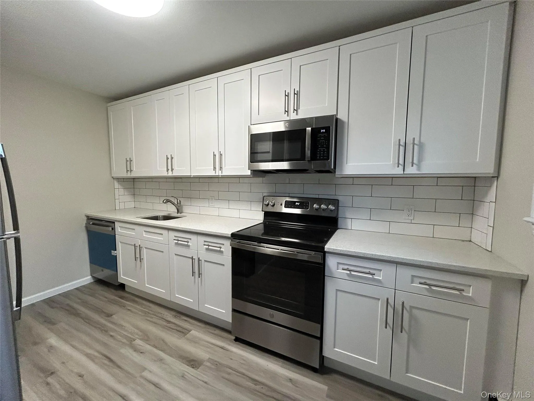 Kitchen featuring appliances with stainless steel finishes, light stone countertops, white cabinets, and light wood-style floors Kitchen featuring appliances with stainless steel finishes, light stone countertops, white cabinets, and light wood-style floors