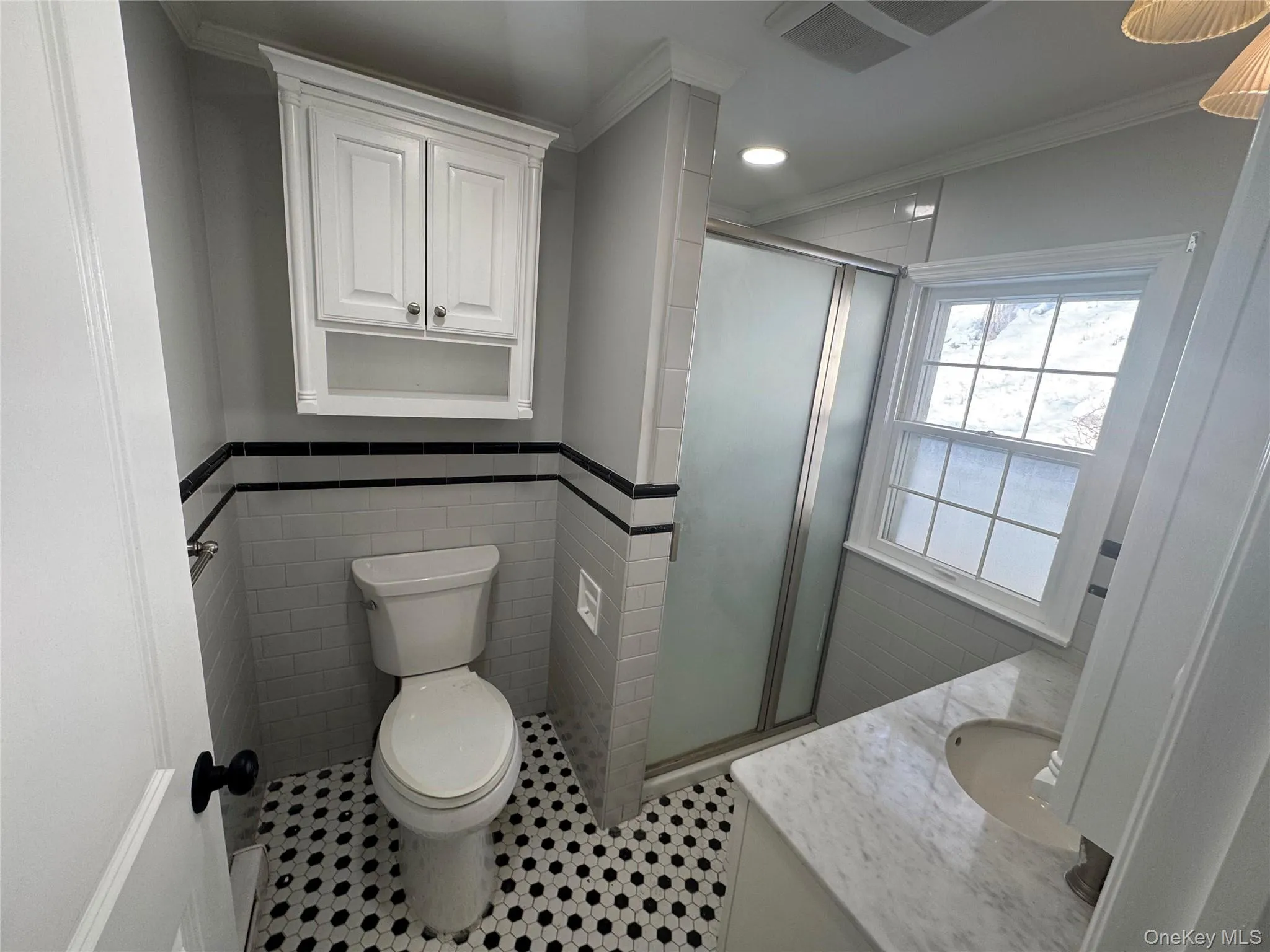 Bathroom with vanity, a stall shower, ornamental molding, wainscoting, and tile walls Bathroom with vanity, a stall shower, ornamental molding, wainscoting, and tile walls
