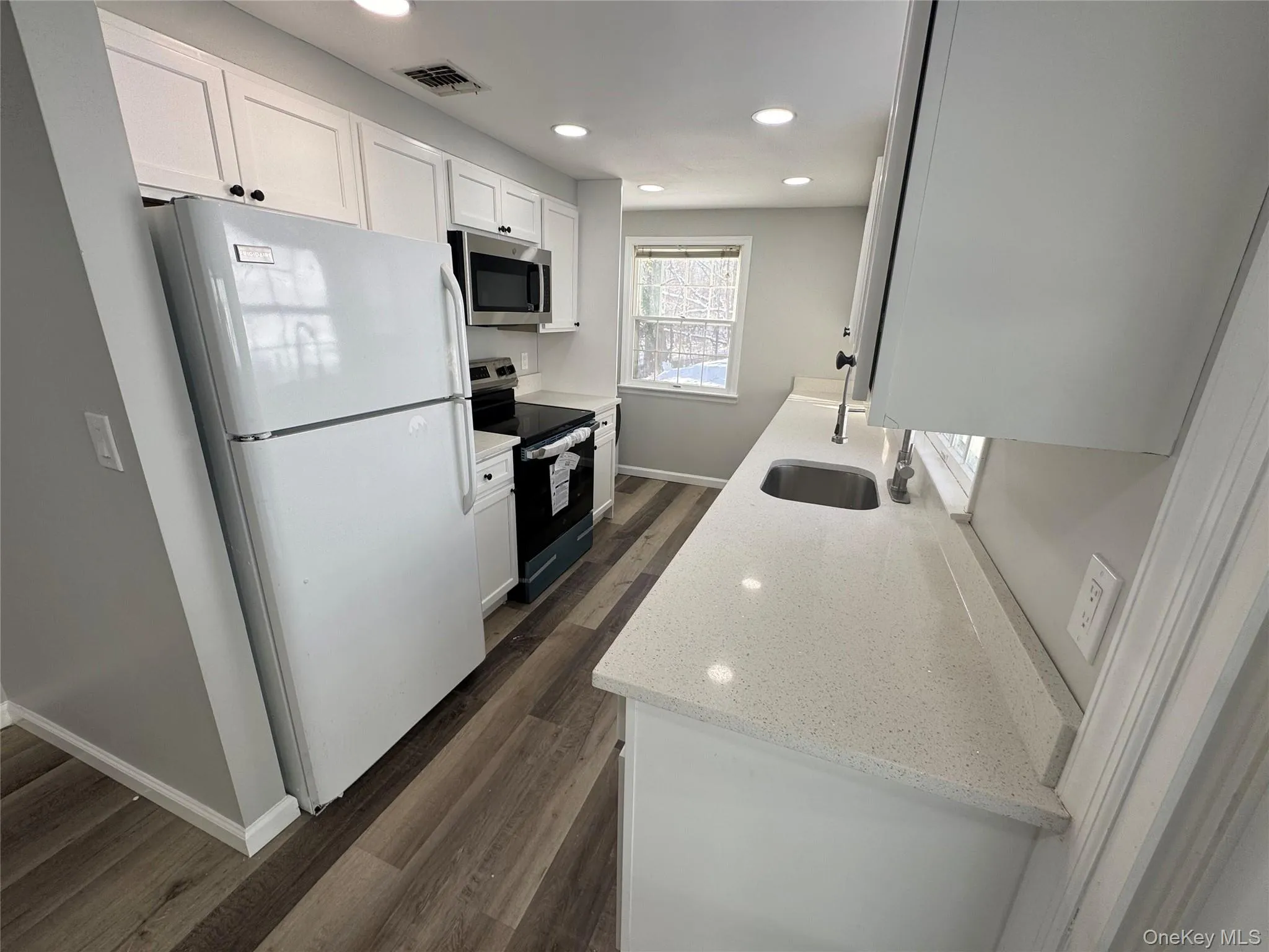Kitchen with appliances with stainless steel finishes, white cabinets, light stone countertops, recessed lighting, and dark wood-style floors Kitchen with appliances with stainless steel finishes, white cabinets, light stone countertops, recessed lighting, and dark wood-style floors