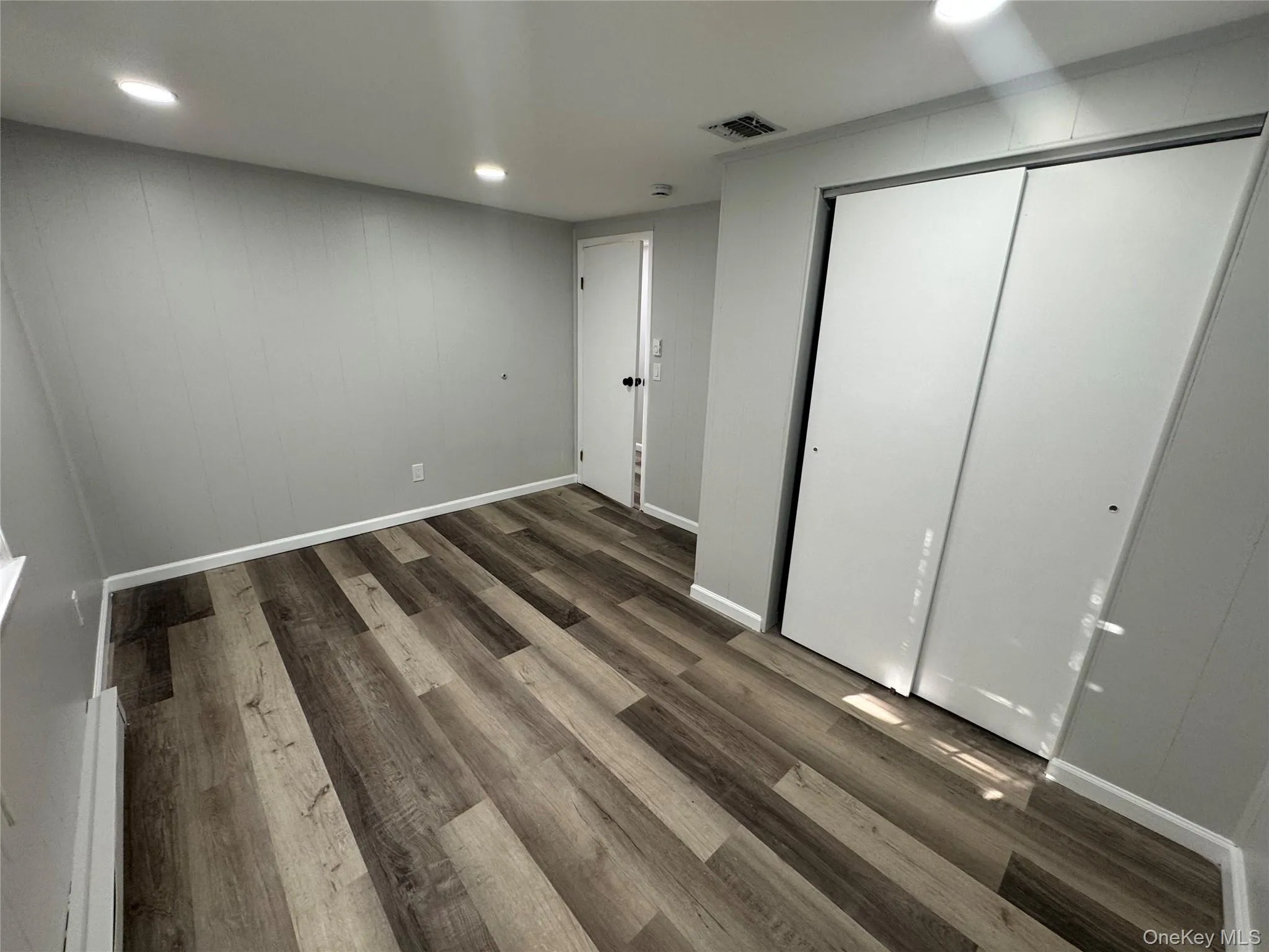 Unfurnished bedroom with recessed lighting, dark wood-type flooring, a closet, a baseboard radiator, and wood walls Unfurnished bedroom with recessed lighting, dark wood-type flooring, a closet, a baseboard radiator, and wood walls