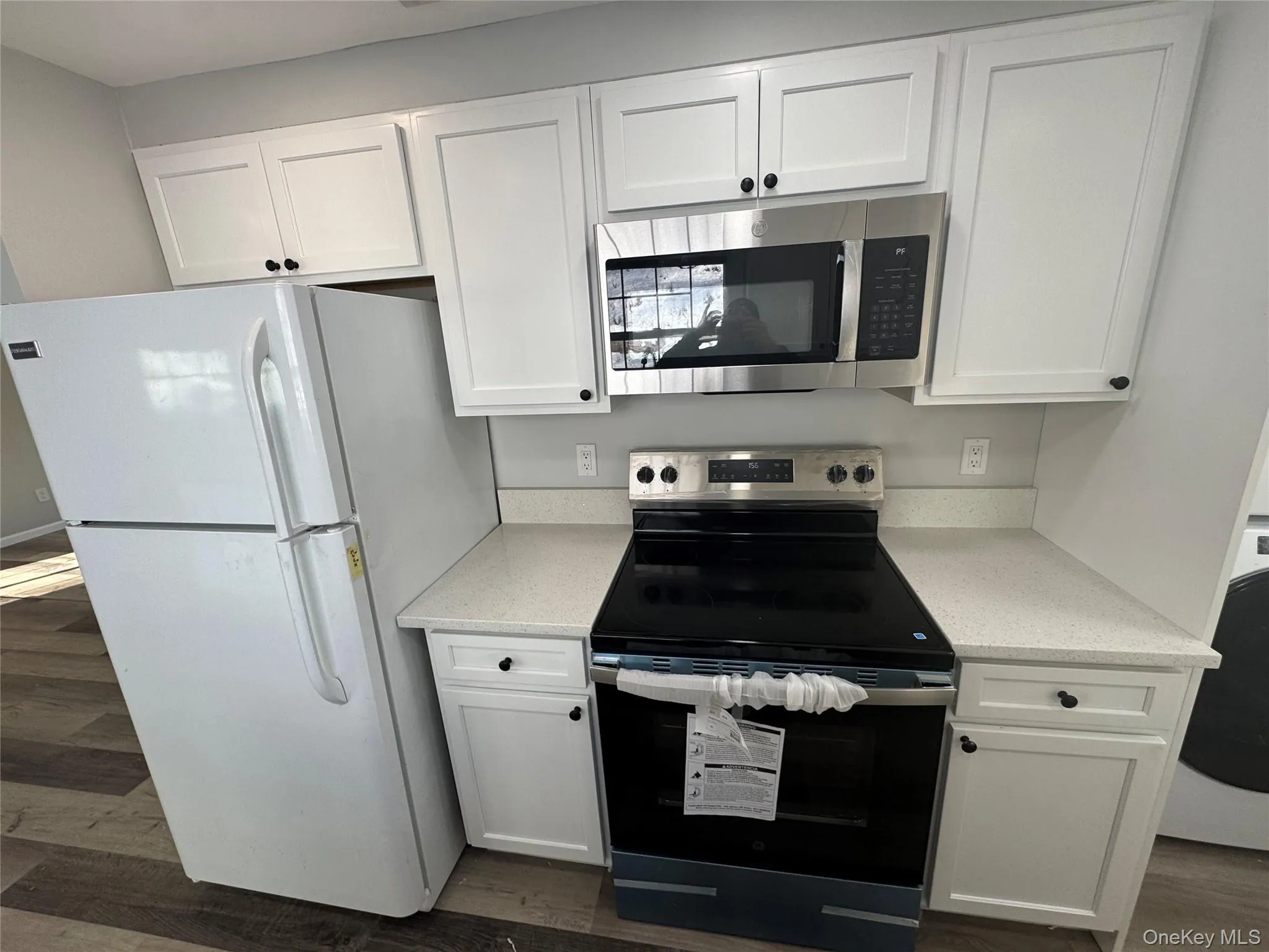 Kitchen featuring appliances with stainless steel finishes, white cabinets, dark wood-style floors, and light stone countertops Kitchen featuring appliances with stainless steel finishes, white cabinets, dark wood-style floors, and light stone countertops